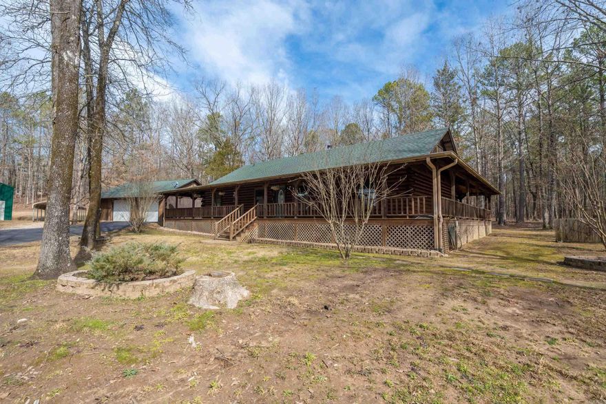 ON THE OUTSKIRTS OF HOT SPRINGS IS AN OUTSTANDING LOG HOME with the backdrop of a park-like, wooded 3 Acre setting!  From the circle drive and wrap around porches to the oversized garage + the car enthusiast's air conditioned DREAM shop, this home deserves your attention.  The main house has vaulted ceilings, a beautiful native stone fireplace separating the family room and kitchen/dining areas.  Hardwood floors are prevalent; and the kitchen offers stainless steel appliances and granite countertops!  At the back door is a lovely patio with grotto that is covered seasonally with voluptuous grapevines.  The square footage includes a 25 x 35 1 Bedroom 1 Bath cottage ideal for guest or mother-in-law quarters.  This location is an equal distance to HWY 70West or HWY 270 West for a easy drive to Lake Hamilton or Lake Ouachita.