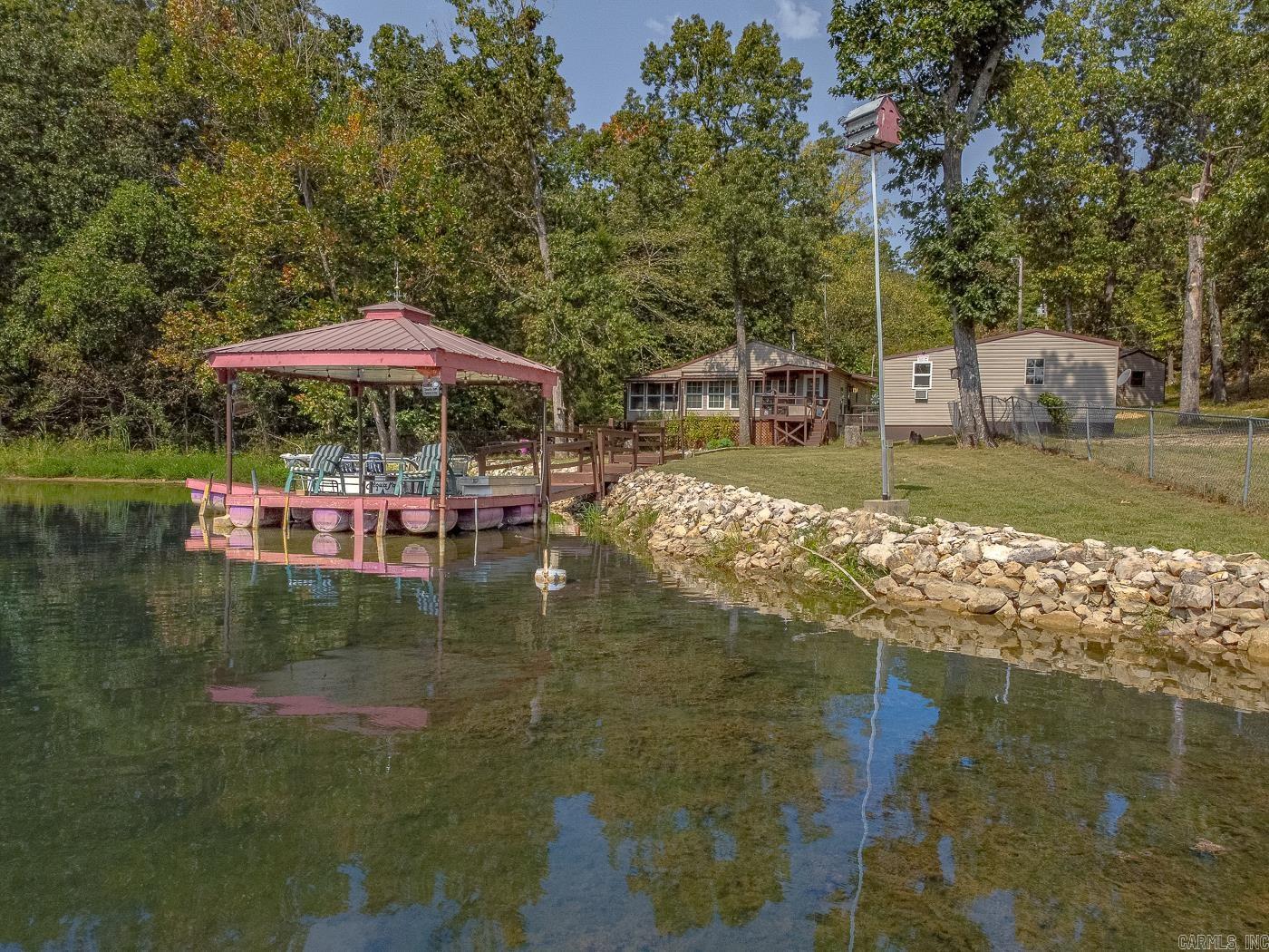 Welcome to Market 21 W Lakeshore Dr. of the West Lake Hidden Valley Sub. in Highland, AR within the Highland School District. Situated on 2 Lake Mirandy frontage lots is a 2012 built Cottage Bungalow wrapped in vinyl, topped w/ a metal roof, and accented by a covered front porch & wood deck. The all electric interior features 1,400 sf of well laid out living space that includes a living room w/ cozy electric fireplace and built in storm cellar, galley kitchen w/ electric range & dishwasher, sunroom w/ wood stove, Master bedroom w/ en-suite w/ walk-in shower & closet w/ barn door, spare bedroom w/ half bath, guest half bath, and laundry room. The grounds feature a 12x12 covered dock w/ electric, 24x40 5 room shop, 20x20 carport w/ 220v and 110v, 12x20 garage w/ electric, 10x24 storage room under the house w/ double door, and fountain. This lake ready property includes a Pontoon boat and 2 Kayaks. The Sellers love the fishing, boating, swimming, and gorgeous lake views the property provides. Conveniently located near favorite local amenities just 10 minutes to Hardy and Ash Flat. Call today to make this house your home, home away from home, or next addition to your rental portfolio.