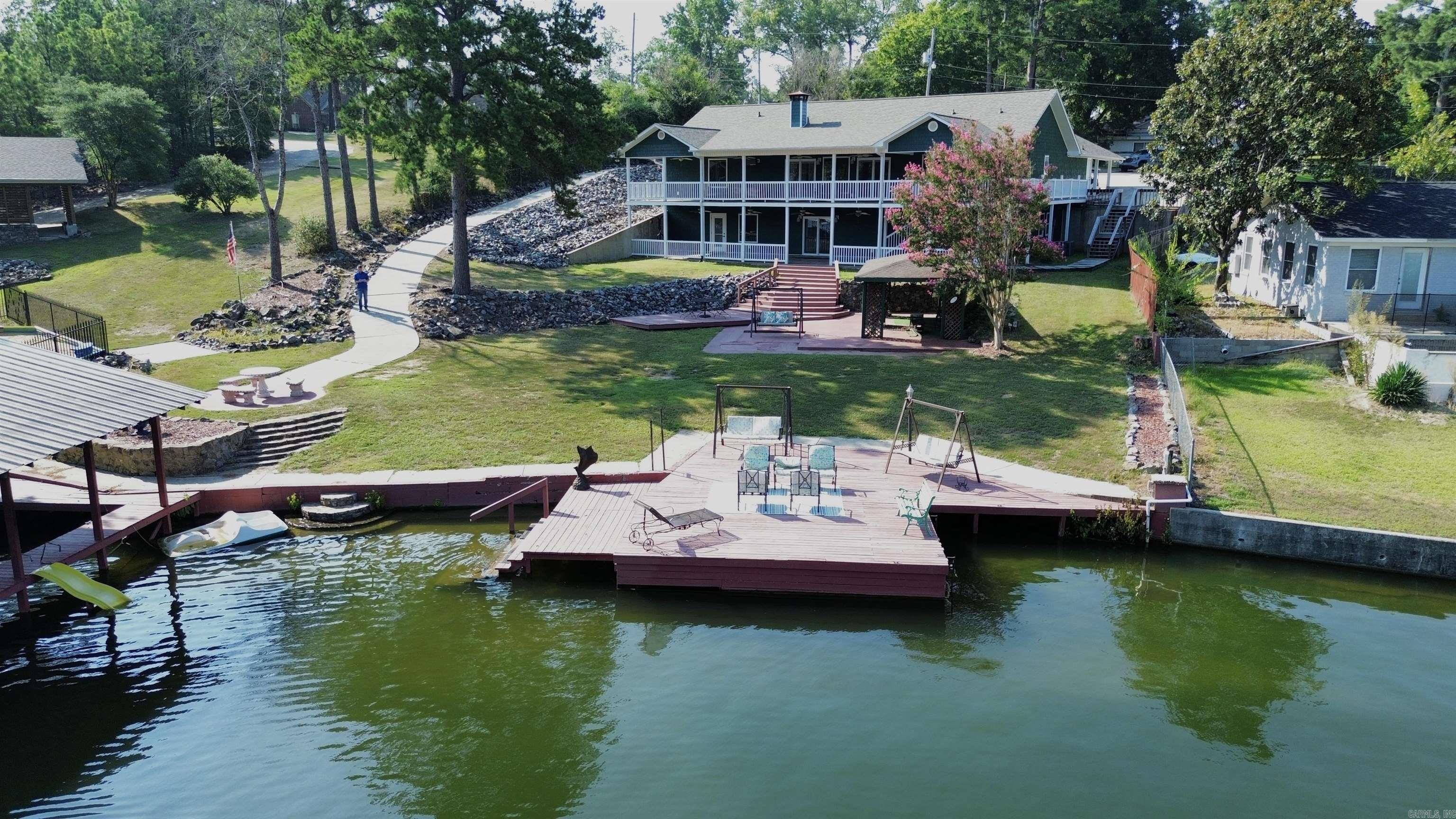 Waterfront Paradise on Lake Hamilton! Experience the ultimate in lakefront living in the sought-after Tanglewood Subdivision. This exceptional property offers two fully self-contained residences under one roof, giving you incredible flexibility — live in one and rent the other, host extended family, or enjoy it all as a spacious single-family retreat. The main level (2,770 sq ft) and lower level (2,310 sq ft) each feature a full kitchen, laundry, generous living and dining areas, a 792 sq ft covered porch, and a private entrance. With separate heat/air units and meters, you control comfort and efficiency for each space. Inside, you’ll find expansive lake views from large windows and glass doors, a main-level primary suite with an unbelievable walk-in closet, a dedicated office with water views, spa-like bathrooms with soaking tubs and custom walk-in showers, and a cozy wood-burning fireplace. Outside is your private Lake Hamilton playground — 150’ of prime waterfront, a 2-stall covered boat dock, oversized swim deck with easy lake access, a charming cabana, and a fully fenced park connected by a paved golf cart path. Two outbuildings and a 1,500 sq ft walk-up attic.