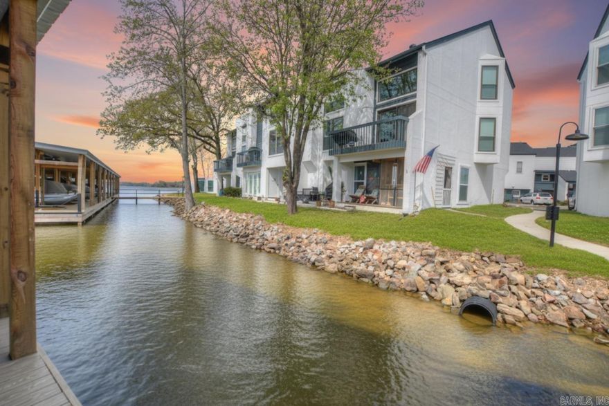 Nestled at the end of Grand Point Drive, the Treehouse Condo community offers a rare, island-like setting surrounded by the serene waters of southeast Lake Hamilton. Developed in 1980, this gated complex provides the expansive green space and quiet privacy that newer developments often lack. With a 30-day minimum rental policy and a reputation for "awesome neighbors," it is the ultimate retreat for vacation owners seeking tranquility.  This two-story, second-floor unit is offered fully furnished and move-in ready. The main level features a primary suite with a walk-out balcony and a cozy living area with a wood-pellet fireplace. The kitchen is fully equipped for entertaining with a standard refrigerator, a counter-height drink fridge, and a dedicated ice maker. Two additional bedrooms and a full bath are located on the second level, providing plenty of space for guests.  The property has undergone extensive recent updates, including a new roof (2025), fresh exterior paint (2024), a rebuilt pool deck (2025), and a resurfaced parking lot (2026). Boaters will love the covered slip with a 10,000 lb. hydraulic lift and recently replaced docks (2024).