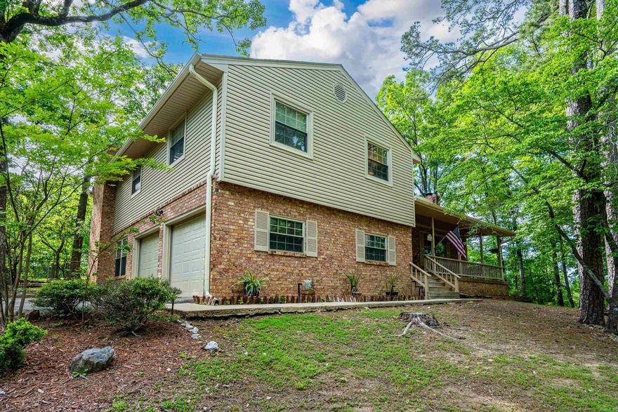 Private 6.28 acres just minutes from Hot Springs-the rare combination of space, privacy and peaceful country living. Enjoy quiet mornings on the welcoming front porch, taking in the natural surroundings. This 2,612 sq. ft. home features 3 bedrooms plus a flexible den currently used as a 4th bedroom. The lower-level den offers a private retreat with a stone wood-burning fireplace, full bath and garage access-ideal for guests or extended living.   The main level includes a bright living room with a large picture window and brick fireplace, flowing into the dining area for a layout that feels both connected and defined. The kitchen features granite countertops, bamboo flooring, custom cabinetry and ample storage.   Step outside to a 20 x 32 patio with pergola, ceiling fan, lighting and custom railing. This outdoor living area overlooks a fully fenced-backyard. and is surrounded by woods on three sides-a peaceful setting where you can often enjoy local wildlife. Privacy, flexibility and room to spread out-all just minutes from Hot Springs.