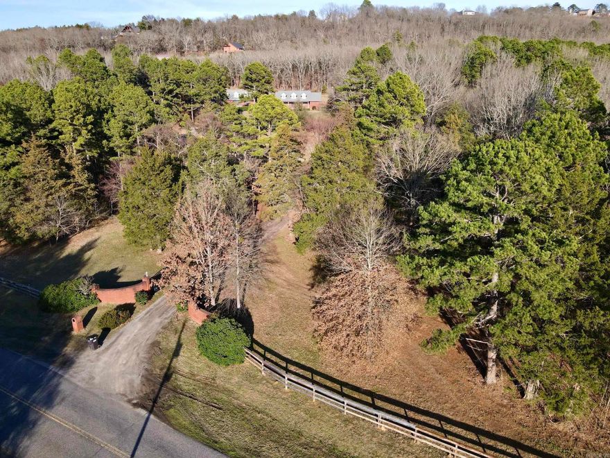 This exceptional 15.32-acre property just outside Russellville, Arkansas offers privacy, acreage, and convenience less than one mile from I-40 on the west side of Crow Mountain with views of Mount Nebo.  Built in 2005, the custom 3-bedroom, 2-bath brick home features 3,106 square feet with a split floor plan, formal and casual living areas, and a spacious family room with wood-burning stove. A separate formal living room and a glass-enclosed sunroom overlooking the landscaped, park-like backyard provide excellent entertaining space and year-round enjoyment.  The kitchen includes custom oak cabinetry with glass fronts, abundant counter space, an eat-in area, and a central island. The oversized primary suite offers large walk-in closets and a private bath.  Improvements include two detached brick garages: a 1,600± sq ft garage with two overhead doors, finished interior, office, and built-in safe room, plus a 1,333± sq ft 220-wired workshop. A hillside storm shelter with electricity adds security. Gated entry, brick columns, fencing, mature timber, small vineyard, and chain-link fenced backyard complete this private yet conveniently located estate.