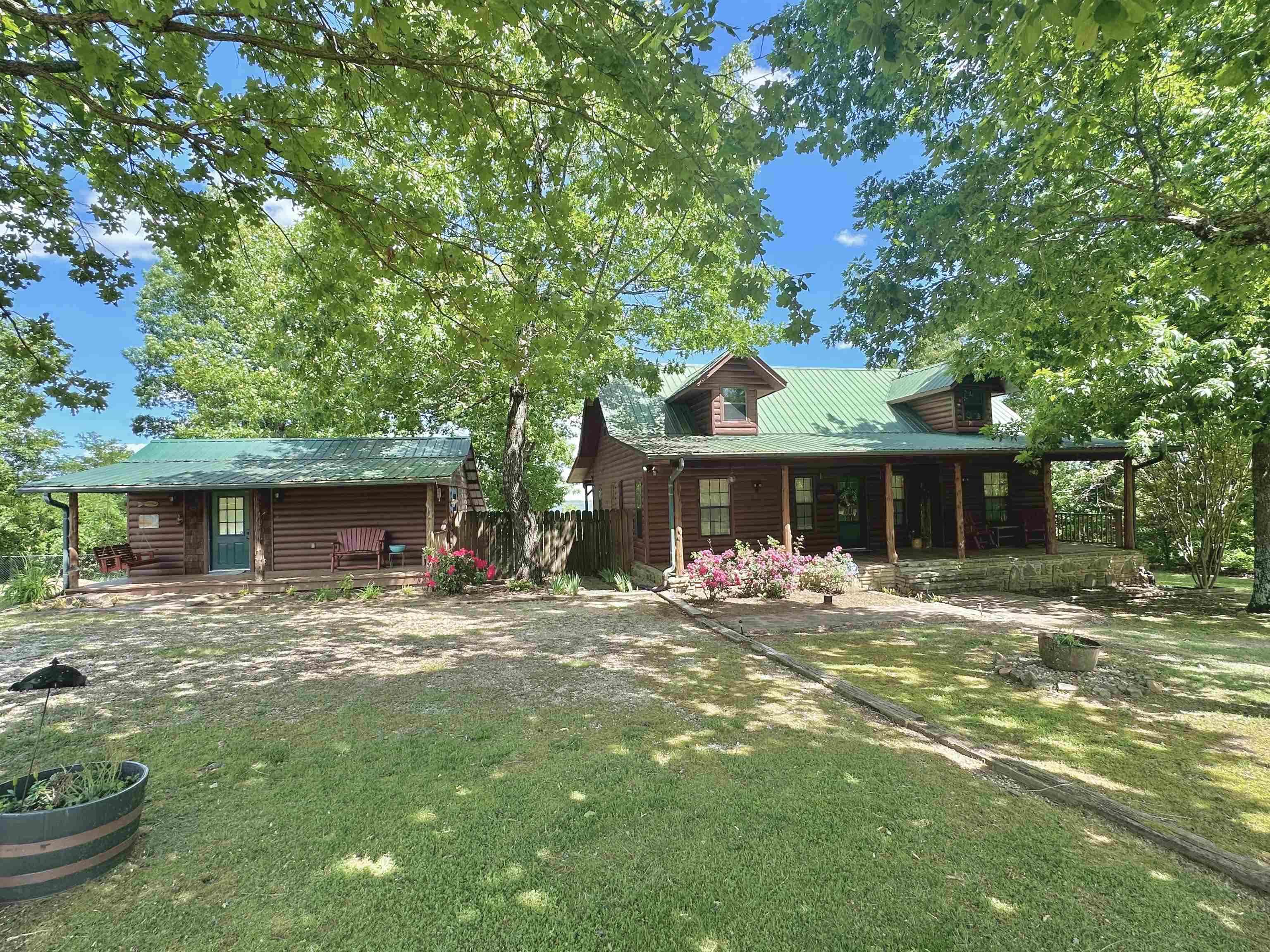 Nestled in the Ozark Mountains, sits this well maintained FULLY FURNISHED Cabin & guest house with an amazing view!! The main cabin features an open living area with tall wood ceiling along with a wood burning stove and a spacious kitchen adjoined by a walk in pantry/laundry room. The master bedroom is also on the main floor with a completely remodeled bathroom. Upstairs is a 1/2 bathroom, open bedroom, and a sitting area/nook. Off the back deck of this home is a large patio area made of stone, built in firepit, and plenty of room for outdoor entertainment. The property also takes in a portion of a shared pond! The guest cabin features 1 bedroom/1 bathroom and makes the perfect guest cabin or vacation rental! The main home has had my updates recently! An added BONUS is an additional lot with a storage building, carport covering, and orchard! This property is beautifully landscaped and very inviting. Located a short drive to Downtown Mountain View!