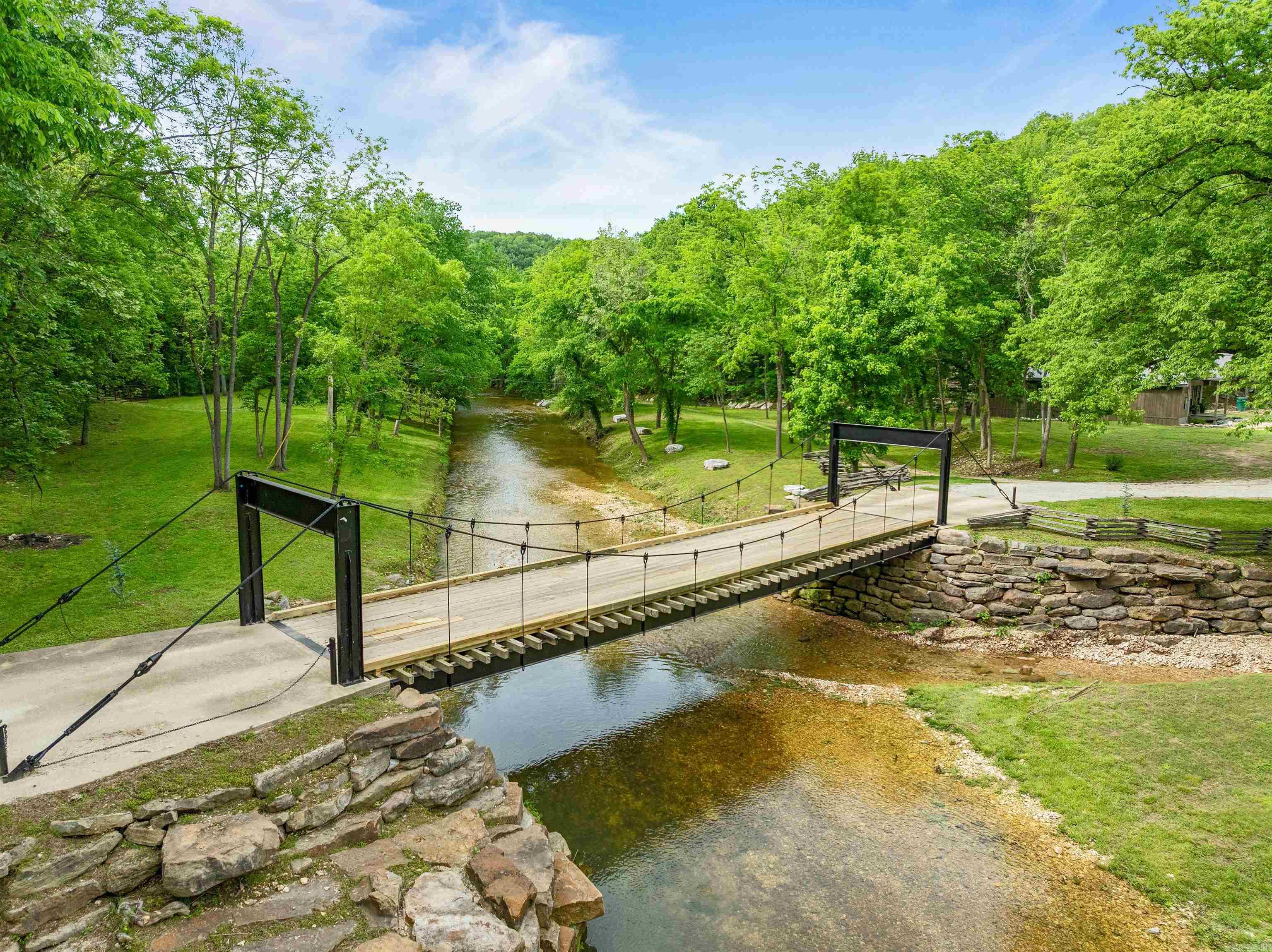 The Creek Cabins at Brush Creek, near the Buffalo River in Marshall, AR, offer a unique retreat amid stunning natural beauty. Set on 40 private acres, the destination features rock terraces, creek side lawns, and a picturesque entrance crossing a flowing creek. It's just 4 miles from the Buffalo River and 15 minutes from the nearest canoe outfitter, with the convenience of town only 3.8 miles away. Operating as a successful short-term Airbnb and enchanting wedding venue, The Creek Cabins provide an unparalleled experience. Each cabin offers a boulder hot tub, surrounded by peace and tranquility. Creeks Edge Cabin is a modern rustic cabin on the edge of Brush Creek, full of amenities and perfect for a home away from home. Dry Creek Cabin, the smallest cabin, features luxurious modern amenities with an open concept living/sleeping area and a full kitchen. Sky View Yurt, perched fourteen feet off the ground, offers a beautiful view of the grounds and Brush Creek. Stones Throw Lodge, the largest cabin at Brush Creek, is just under 3,000 sqft. It offers 3 bedrooms, 2 full baths, a beautiful living and dining area, and a private deck with ample seating, perfect for larger parties.