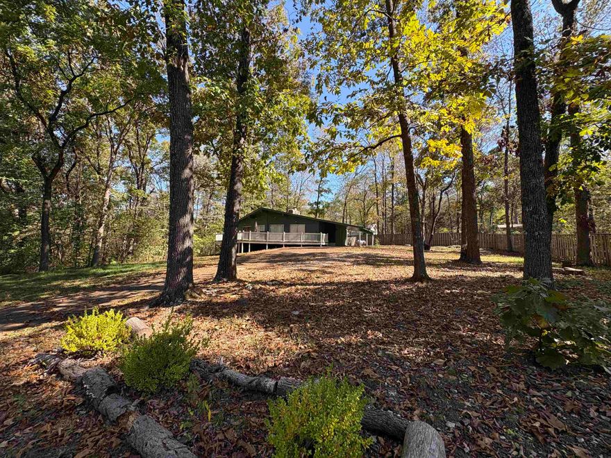 Tucked among the trees overlooking Lake Cherokee, this 3-bedroom, 2-bath holiday-style cottage feels like stepping back into a simpler time — the kind of place where mornings start with coffee on the deck and end with the glow of the stone fireplace or sitting amongst the trees by the fire pit. Vaulted ceilings and rich wood tones give the home a cozy, old-school character that you just don’t find anymore. The open-concept living, dining, and kitchen area makes gathering effortless, while sliding glass doors in both the primary suite and guest bedroom invite in soft lake views and natural light. The primary suite is privately tucked on one side with its own bath and laundry, offering separation from the additional bedrooms. Outside, a fenced yard and extra lot give space to breathe — perfect for pets, gardening, or just relaxing under the trees. Whether it’s a full-time retreat or a nostalgic weekend getaway, this cottage blends vintage charm with lakeside living in the heart of Cherokee Village.
