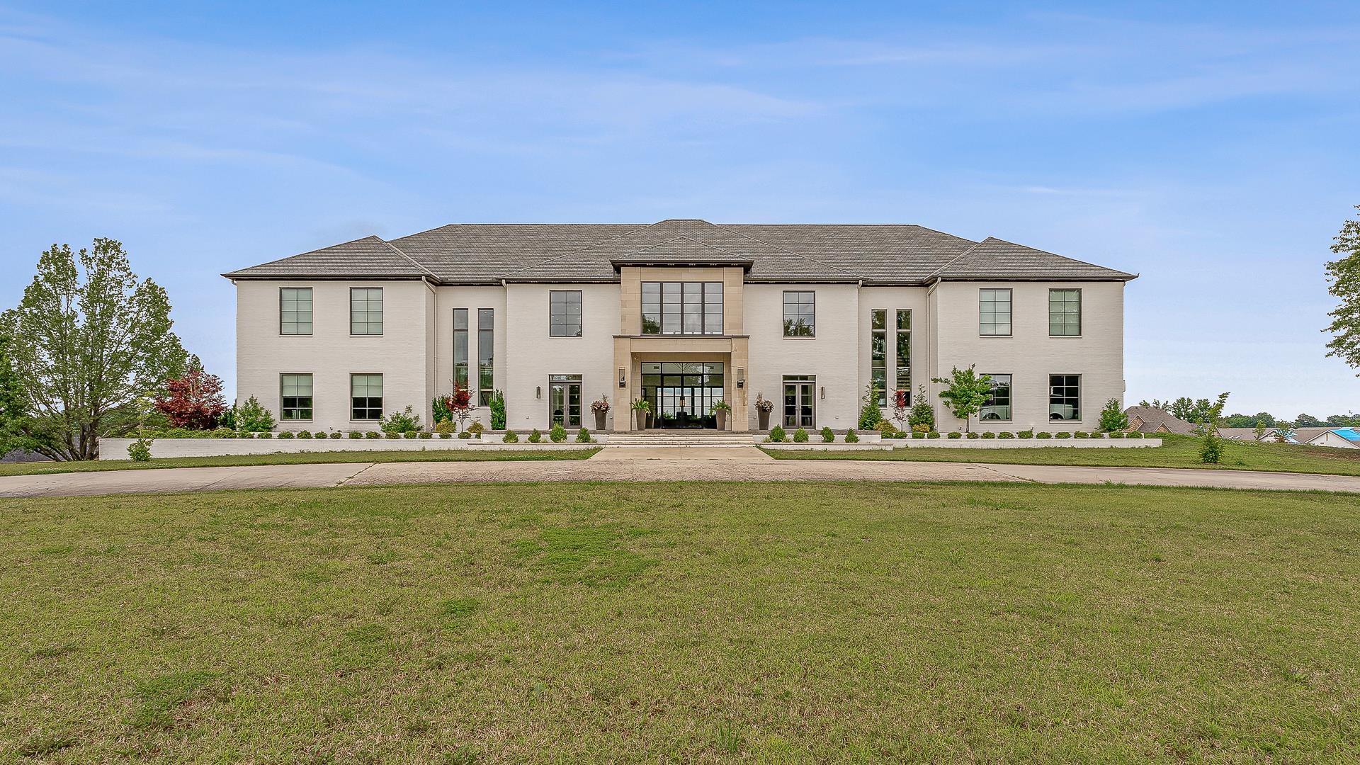 A showcase of modern elegance, this 6-bed, 7.5-bath contemporary estate offering three floors of luxury living on 12.3 acres across from Paragould Country Club golf course. Designed with sophistication and comfort in mind, the home features soaring ceilings, Control4 automation, and an indoor half-court basketball court with full bath. The main level stuns with a Thermador and Sub-Zero chefās kitchen, gas range, double ovens, two dishwashers, and a scullery with warming drawer, microwave drawer, and extra refrigeration. A wet bar with Sub-Zero wine fridge and cooler drawers enhances entertaining. The theatre room includes a private kitchenette. The primary suite is a retreat of its own, with radiant heat flooring, steam shower, a see-through fireplace, and a backlit onyx feature wall behind the soaking tub. Downstairs, enjoy a spacious family room, home gym, full bath, sauna-ready space, and a secure safe room with a Brown Safe Company vault door. Outdoor amenities include a heated gunite pool with spillover spa, screened firepit lounge, outdoor kitchen with fireplace, and upper-level patios.