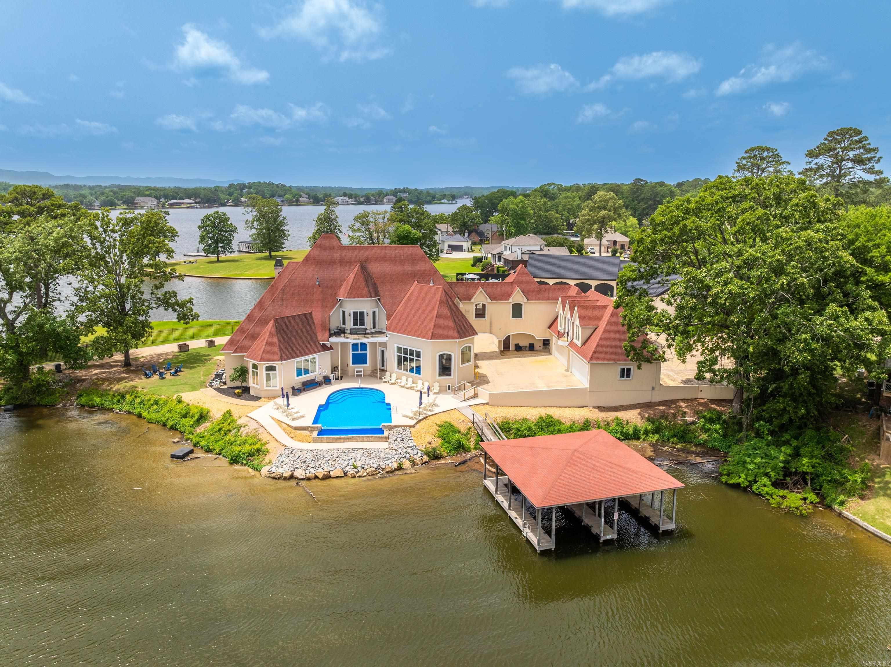LUXURY LAKEFRONT ESTATE ON LAKE HAMILTON ā An Entertainerās Dream & Investment Goldmine! Welcome to your own private peninsula on the sparkling shores of Lake Hamilton! This well-appointed, FURNISHED 7-bedroom, 7.5-bath, 8,056 sq ft lakefront masterpiece offers panoramic water views from every room and an unmatched level of luxury, comfort, and opportunity. Situated on 241 feet of prime waterfront, this estate is designed to impressāfrom the grand entrance to the infinity pool overlooking the lake. Inside, you'll find a chefās dream kitchen complete with gas and electric stoves, an indoor grill, and high-end finishes throughout. Every detail has been thoughtfully curated: a spacious master en-suite that feels like a private retreat, guest quarters for extended stays, a media room for movie nights, and three fireplaces to cozy up on chilly evenings. An elevator provides easy access to all levels, and a 4-car garage ensures plenty of space for guests or lake toys. Currently operating as a top-performing vacation rental which sleeps 24 guests and has the flexibility of being your full-time residence, weekend retreat or investment property. Includes two-stall covered boat dock.