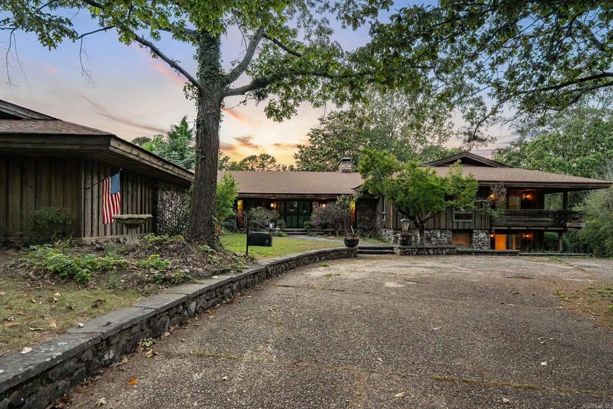 Distinctive mid-century modern home set on 7.7 acres with a gated drive, built under advisement of noted Arkansas architect E. Fay Jones, offering 5 bedrooms and 5.5 baths. The rock and frame exterior welcomes you into a center hall with slate floors and rock flanked circular staircase to lower level. A formal living room with fireplace, built-ins, and sliding doors opens to a covered patio and flows to the formal dining room. The spacious Den/family room features wood-beamed ceilings, an impressive rock fireplace, and outdoor access. Oversized kitchen includes bar area, pantry, double ovens, a large central island with grill and dual cooktops, plus an informal dining area. Laundry and office/craft room as well. The primary suite is expansive with a dual layout bath, walk-in shower, tub and generous closet space. Two additional bedrooms share a bath and deck access. Lower level leads to a bonus game room with wet bar, fireplace, and outside access, along with two bedrooms, each with a private bath. Covered porches and decks, an outbuilding/potting shed, and a large garage with storage complete the property. Truly one of a kind.  Come see!