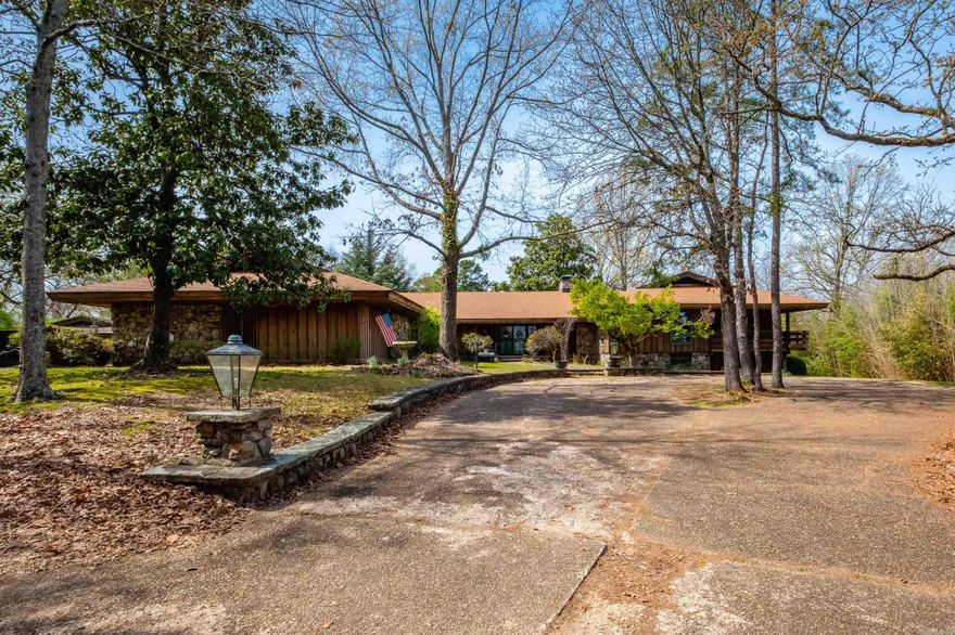 Distinctive mid-century modern home set on 7.7 acres with a gated drive, built under advisement of noted Arkansas architect E. Fay Jones, offering 5 bedrooms and 5.5 baths. The rock and frame exterior welcomes you into a center hall with slate floors and rock flanked circular staircase to lower level. A formal living room with fireplace, built-ins, and sliding doors opens to a covered patio and flows to the formal dining room. The spacious Den/family room features wood-beamed ceilings, an impressive rock fireplace, and outdoor access. Oversized kitchen includes bar area, pantry, double ovens, a large central island with grill and dual cooktops, plus an informal dining area. Laundry and office/craft room as well. The primary suite is expansive with a dual layout bath, walk-in shower, tub and generous closet space. Two additional bedrooms share a bath and deck access. Lower level leads to a bonus game room with wet bar, fireplace, and outside access, along with two bedrooms, each with a private bath. Covered porches and decks, an outbuilding/potting shed, and a large garage with storage complete the property. Truly one of a kind.  Come see!