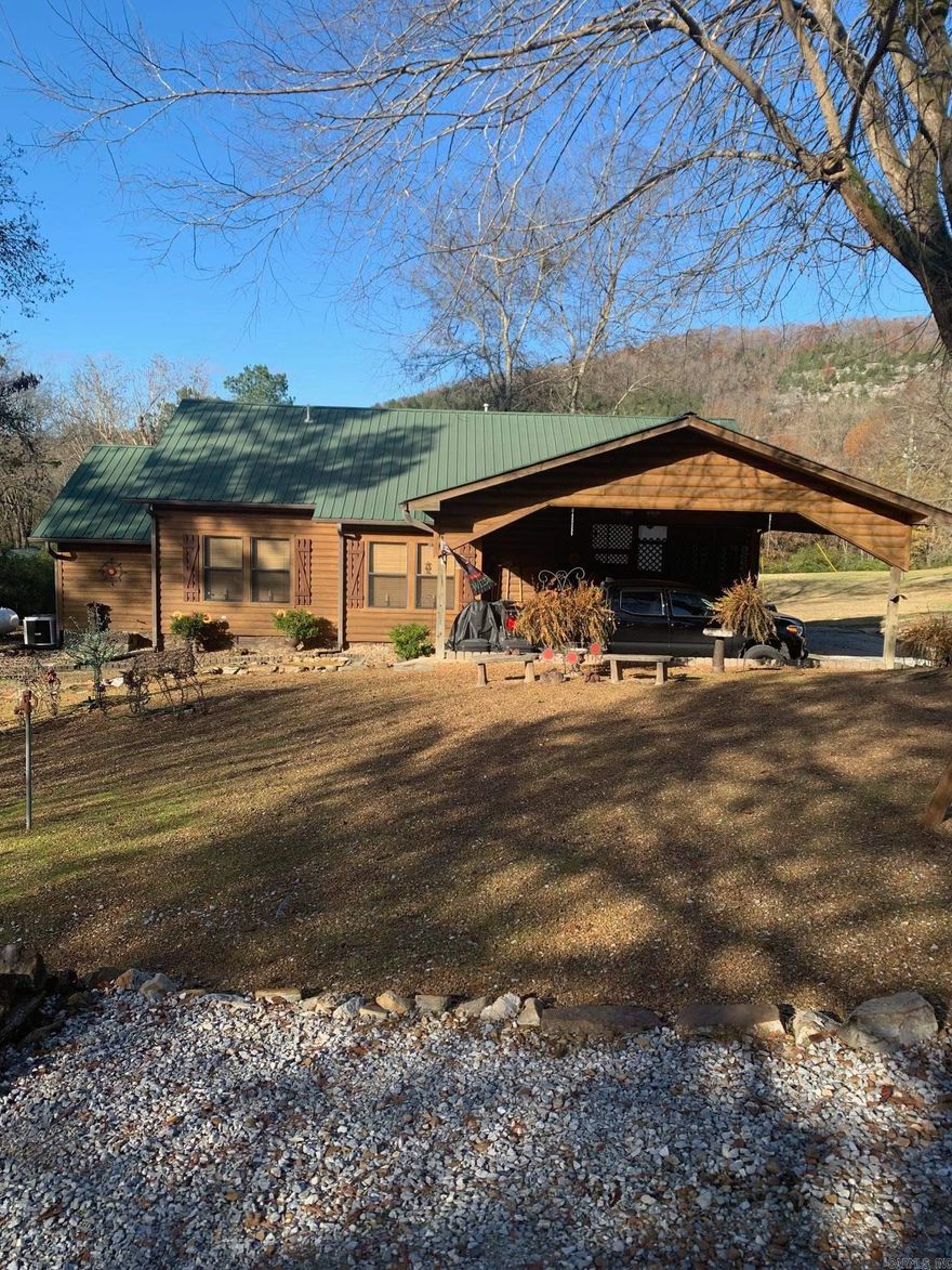 No. 25002 Lodge-style charm near the White River!  This 2 bed, 2 bath home offers 1,492 sq ft with an office that could be a 3rd bedroom, spacious kitchen, two dining areas, cozy living room, and a den with a wall of windows. Enjoy outdoor living with a screened-in porch, double post-and-beam carport, 2 storage buildings, fenced enclosure for pets, and beautifully landscaped grounds with gated drive.  Home underwent a complete remodel in 2010 with new electrical, plumbing and so much more. Practical features include city water, an old water well, gutters & drain system, storm shelter, and propane. Set back from the highway, the long front lawn provides privacy and reduces road noise. All this less than 5 minutes from the White River and the historic Swinging Bridge at Sylamore Creek! Perfect as a full-time home, second home, or VRBO. Seller will consider a one-year lease back. Don’t miss this rare opportunity to own a versatile property in the heart of the Ozarks.  $389,900.00