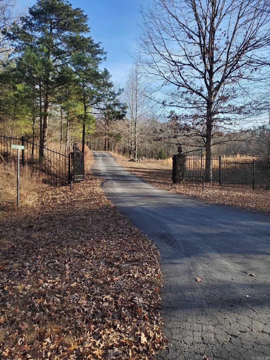 Wooded Country Estate.  7.71 Acres in a great country location about 5 miles from Mena.  Attractive gate entrance opens to asphalt paved driveway leading by a beautiful stocked pond to the homesite on the hill.  It looks out to the near mountains to the north and also to the far mountains to the west.  About the loveliest sunset that can be found (see pictures).  Heavy sloping property with mature hardwood trees.  The present dwelling is a 300 square foot building, due to the beautiful home being destroyed in a fire.  Most of the foundation and rock veneer and approach are preserved, and construction related persons have said the home can be rebuilt there.  Also on the premises are a 2 car garage, partial fencing and storage container.  Acres of rugged country further down the road and into the Ouachita National Forest, with trails for ATV and Horseback Riding.  Lots of deer and turkey and possibly some bears in this country.