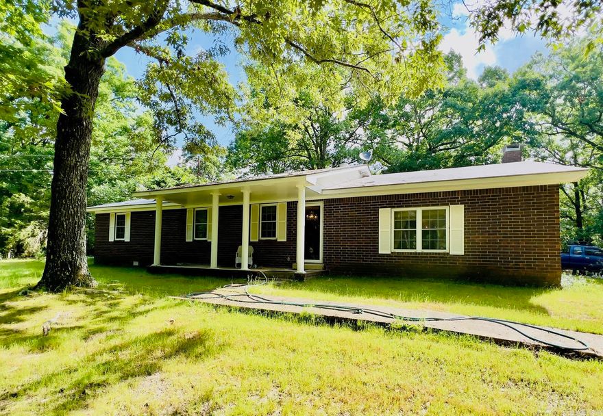 Spacious brick home with beautiful large shade trees in private location just off paved county road. You're going to love this 1922 sq ft home offering a large living area with brick accent wall, woodburning fireplace with insert and beamed ceiling. Well-arranged kitchen with ample cabinets and breakfast bar. Designated dining area, den, nice sized bedrooms, laundry room, roomy full bathroom, currently being updated. You'll appreciate both public water, well, natural gas, septic on property. Septic system inspected and pumped in 2025. Central Heat & Air 5 yrs old.  14x45 RV carport with slab, electric, dump station for convince .  18x30 shop with vehicle lift, spray insulation, heat & air.  Nice outbuilding with electric. Must see property.
