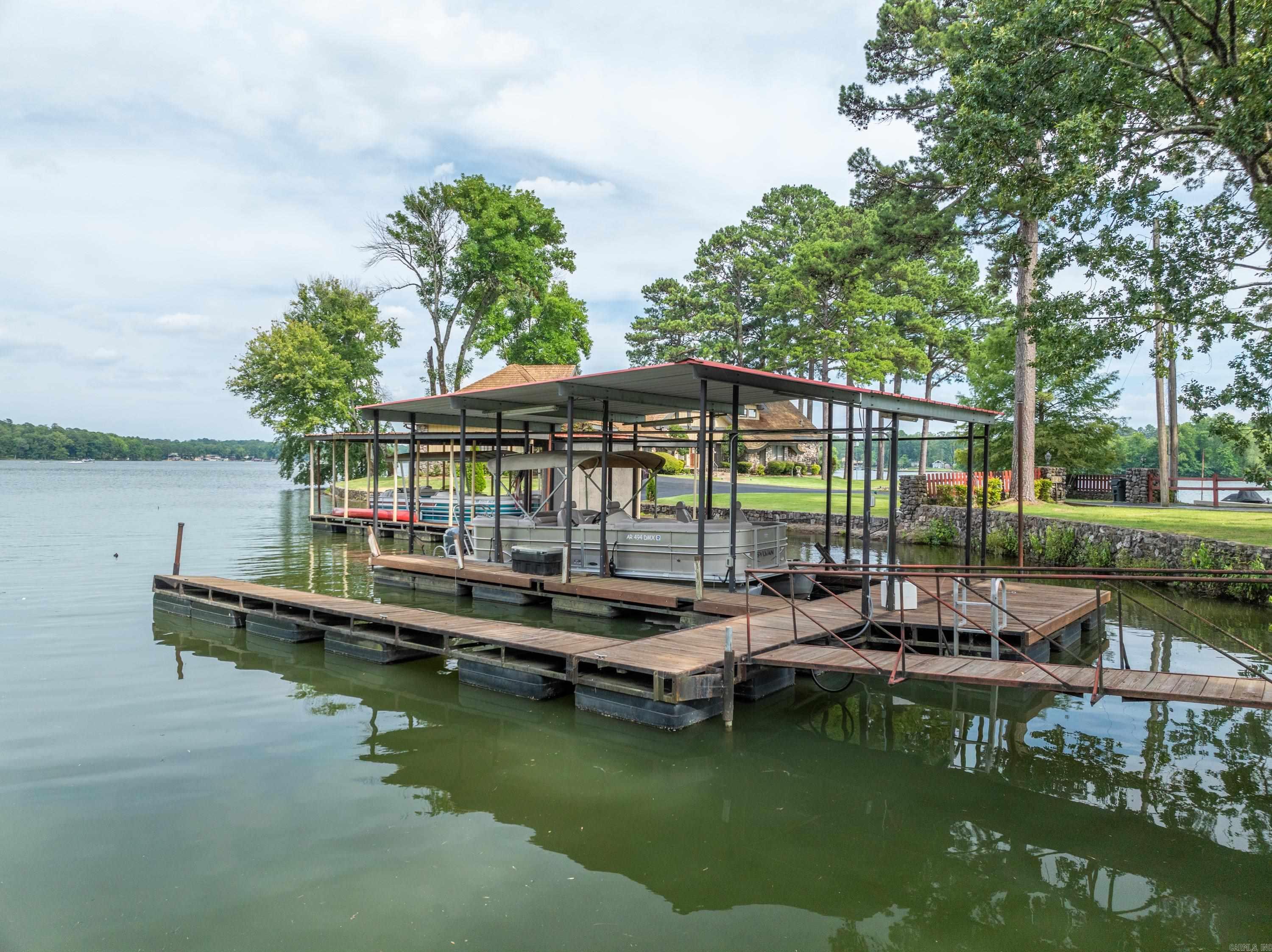 Discover your dream home in this stunning 3-bedroom, 2-bathroom residence nestled in a highly sought-after area of Lake Hamilton. Boasting an open floor plan, this home offers a spacious and inviting atmosphere perfect for both relaxation and entertaining. The large kitchen, complete with dining space, seamlessly flows into a separate bar area, making it ideal for hosting gatherings. Enjoy lake views from the living room and dining room, or step outside onto the covered deck to savor the sunrise. The level lot ensures an easy walk to the dock, with minimal steps throughout the property, enhancing accessibility and convenience. Water enthusiasts will be delighted by the 2-stall boat dock, situated in protected water with little wave action, ensuring your boats stay safe and secure. With an impressive 174 feet of frontage, you'll have ample space to enjoy all the water activities Lake Hamilton has to offer. A charming guesthouse on the property provides an additional bedroom and bathroom, perfect for mother-in-law quarters, a man cave, or accommodating visitors making the total accommodations 4 br 3 BA. 2547 sq ft includes the guest cottage footage.