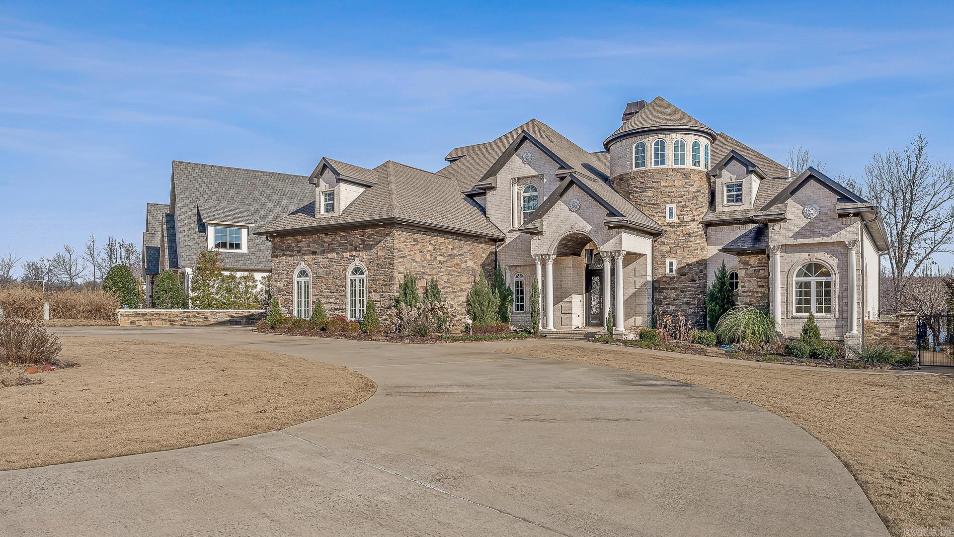 Welcome to 2064 Sloan Lake Dr. in Jonesboro, AR, a stunning 5-bed, 6.5-bath custom-built home with 6,042 sq. ft. of luxury living space. Located in the prestigious Sloan Lake Estates, this home offers breathtaking lake views and exceptional craftsmanship. The grand entry features a spiral staircase, leading to a spacious living room with floor-to-ceiling windows framing the lake and pool. The gourmet kitchen boasts custom cabinetry, a wet bar, and a striking glass tile backsplash. The family room offers a built-in entertainment center and access to the covered patio with an outdoor kitchen, gas fireplace, and poolside full bath. The luxurious primary suite includes a private balcony, spa-like bath, and walk-in closet doubling as a safe room. Upstairs, three bedrooms with en-suite baths, a media room, and a third-floor fifth bedroom complete this home. Additional features include a 3-car garage and beautifully landscaped grounds. Don’t miss the opportunity to own this lakeside masterpiece—schedule a showing today!