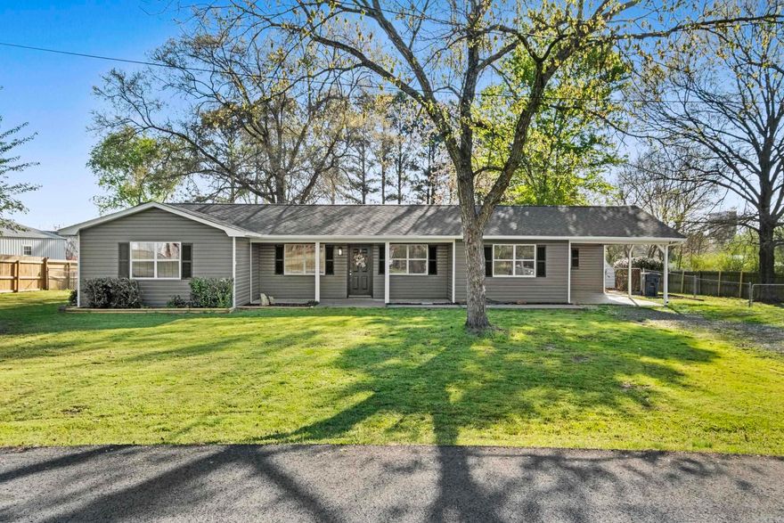 Remodeled 3 bed, 2 bath home with sunroom and functional outdoor space. Interior features include an open floor plan, updated kitchen with island, stainless appliances, and solid surface countertops. White cabinetry with updated hardware, recessed lighting, and tile flooring in kitchen areas. Living spaces include wood-look flooring and ceiling fan. Primary bath offers double vanity and walk-in shower. Sunroom provides additional living space with backyard access. Exterior includes covered front porch, covered patio/pergola area, and detached carport/storage structure.