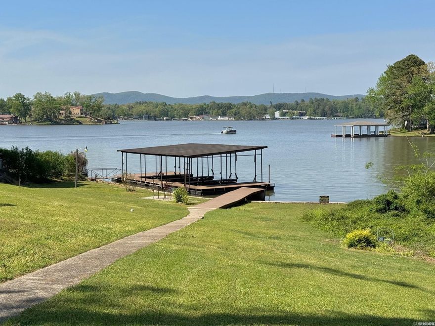 Escape to a tranquil lake oasis on Long Island Drive, one of the most sought-after locations on Lake Hamilton. Enjoy breathtaking main channel views from this exceptional property, boasting over 100' of lake frontage and a THREE-slip covered boat dock.  With two separate houses and a guest cottage, there's plenty of space to accommodate a large crowd. And with just shy of an acre of land, there's plenty of room to build another house on the property. The main house has 3 bedrooms and 3 fully remodeled baths.  The guest house has 2 bedrooms and 1 full bath. All new roofs and HVAC units were recently installed. The updates throughout provide a fresh and modern touch, complementing the timeless mid-century charm. This property has been used as a successful short-term rental for several years.  Location is outside the city limits, so no STR permit is required. All furnishings will convey to the new buyer.