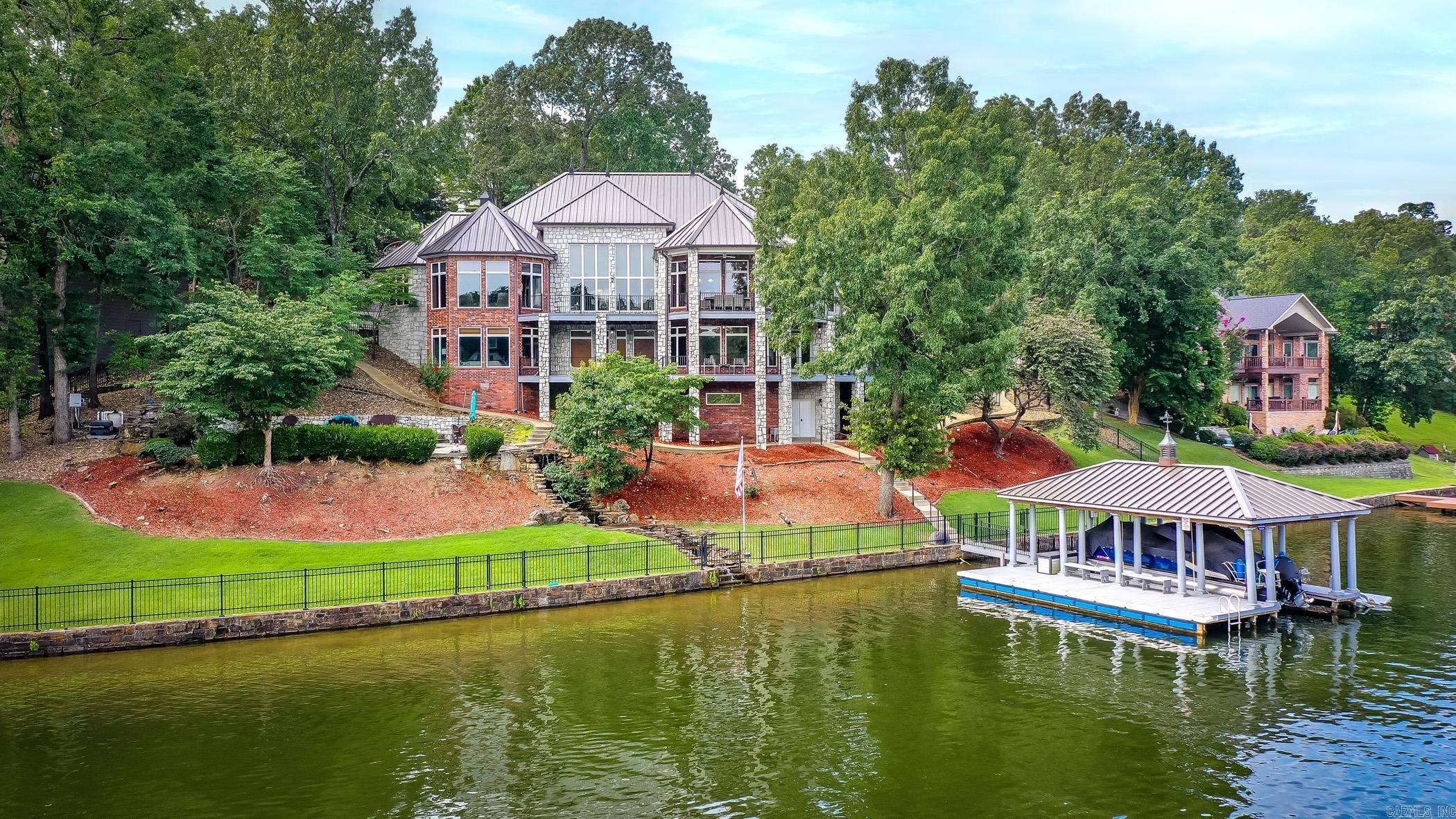 Welcome to 81 Stonegate Terrace, luxury made lakeside. This property sits on 2 lots in a beautifully maintained gated neighborhood with many amenities like the private boat ramp, storage, pool/pool house & basketball/tennis court. The main level will amaze you with the open concept living room, dining room, chefās kitchen offering floor to ceiling views of the lake. Across from the kitchen youāll find the spacious primary with a sitting area, a private office, as well as upper deck & media room access. Downstairs boasts 3 large bedrooms with walk-in closets, full bathrooms & access to the lower deck. This home has abundant storage with two bonus rooms located downstairs. The picture-perfect heated pool with waterfall feature overlooks your private dock with lift and tandem jet-ski dock. The heated/cooled gym/ flex space is located under the house along with a storage room. This stunning home features a whole house generator, new metal roof on both the house & dock, as well as a large attic over the garage. 81 Stonegate is being sold furnished (minus personal items) and truly encompasses the best of lake living without compromising on space and sophistication.
