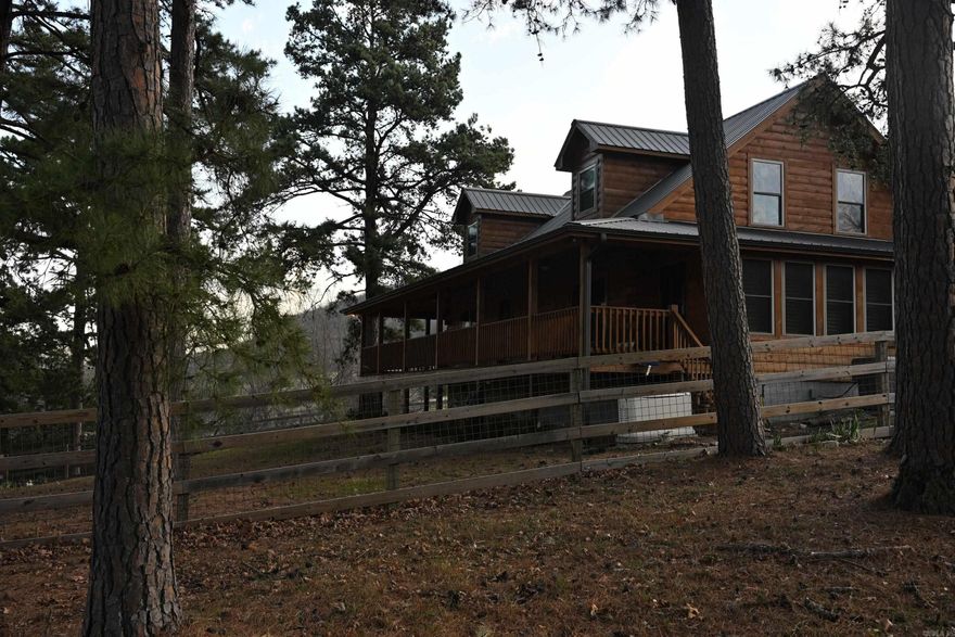 Welcome to a beautiful custom-built log home on 89± acres overlooking Bear Creek Valley, blending craftsmanship with the natural beauty of the Ozarks. This 3-bedroom, 2.5-bath home offers privacy, comfort, and outdoor adventure in a stunning setting. Inside, the great room features vaulted ceilings and a striking two-sided wood-burning fireplace. Hand-scraped hickory and tile flooring add durability and style. The kitchen boasts custom knotty alder cabinetry, granite countertops, and ample workspace, with a covered patio just off the dining area for relaxing or entertaining. The main-level primary suite includes a walk-in shower, soaking tub, and double vanity, plus a sunroom with access to the wraparound porch. Upstairs offers two bedrooms, a full bath, and a versatile loft. Enjoy expansive porches, a firepit, and a partially fenced yard. The land includes wooded acreage and pasture, abundant with wildlife. Additional features include a 2-car garage, 24x40 insulated shop, whole-house propane generator (500-gallon tank), Ecosystem water filtration system, Highway 27 frontage, and fiber internet. Located near Marshall, the Buffalo National River, and an 1 1/2 from Branson, Mo.