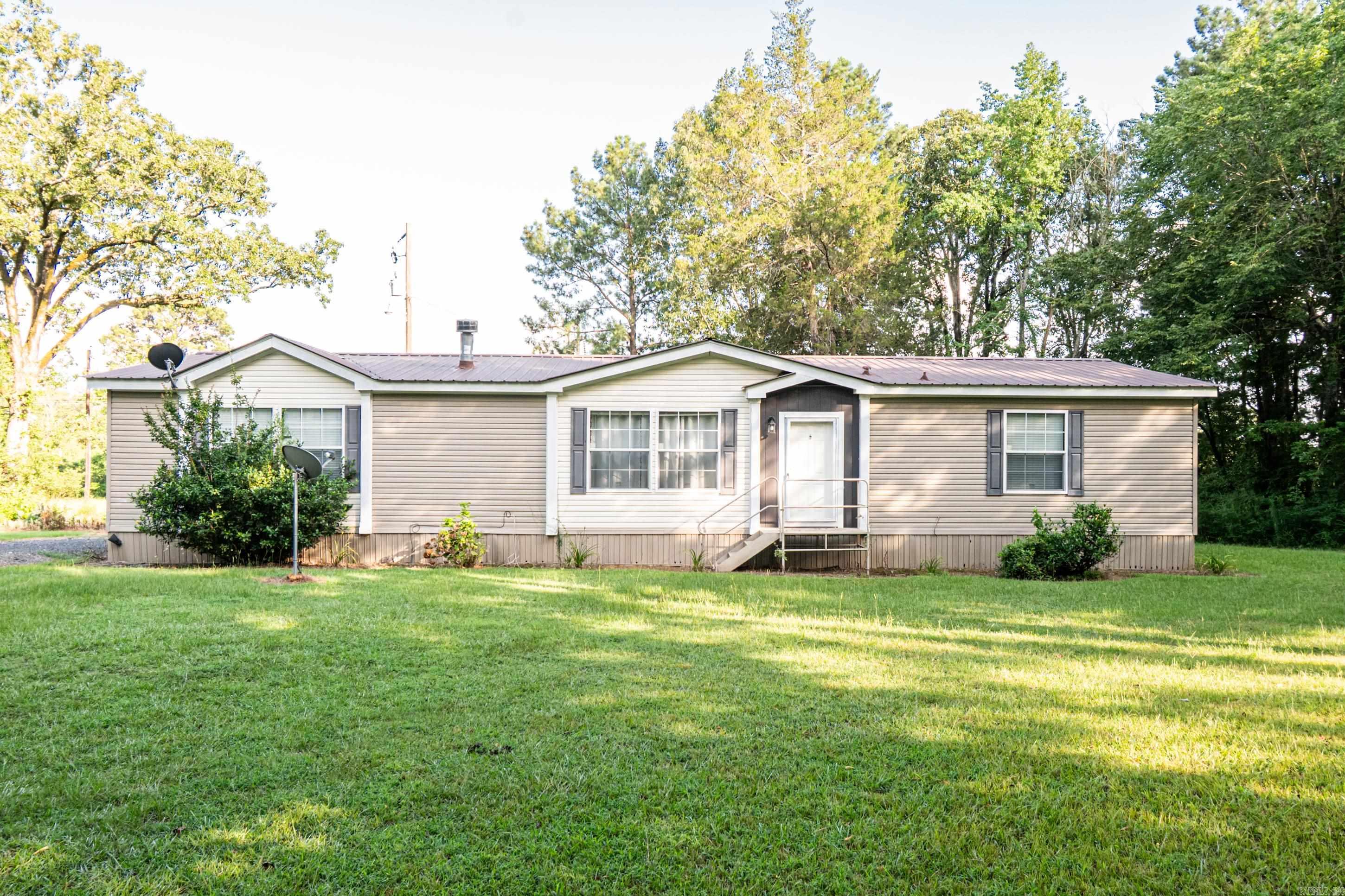 This well-kept 3 bed, 2 bath mobile home sits on a 14.99-acre property, split between two separate parcels—offering space and future potential. Tucked back off a gravel driveway, the home is surrounded by mature woods, creating a peaceful and secluded setting while still being easily accessible. Step inside to an open-concept interior with rich brown and darker finishes that bring warmth and character to every room. The primary bedroom and bathroom are oversized, featuring ample space for furniture, storage, and relaxation. The second and third bedroom make this home ideal for small families, guests, or even a home office setup. Outside, enjoy the expansive deck—perfect for grilling, gatherings, or taking in the views. There’s also a covered parking area to keep your vehicle protected from any weather damage. Whether you're looking for a peaceful homestead, a weekend getaway, or land with room to grow, this property offers it all. Located in a great area with a quiet rural vibe, but still close enough to town or the interstate for convenience, this is a rare opportunity to own land, privacy, and a move-in-ready home all in one.