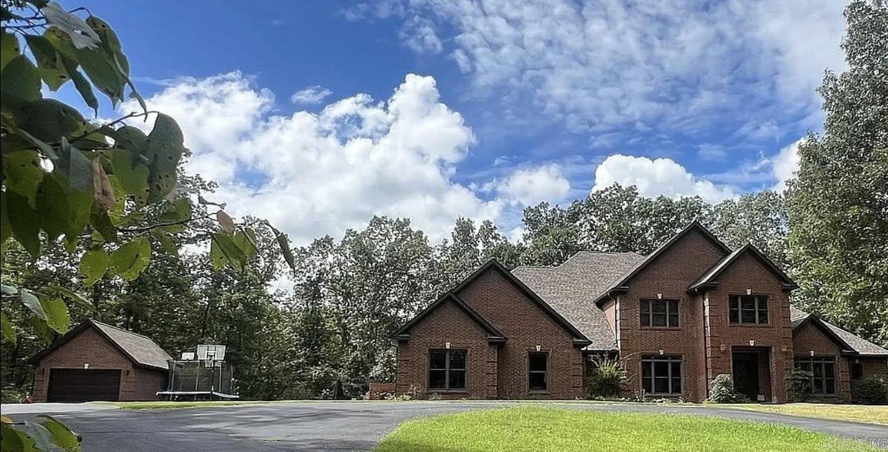 Woodland Hills prestige meets Ozark seclusion in this luxury brick estate on 7 + gated acres bordering protected Ozark Folk Center land—yet still inside Mountain View city limits. A custom solid-oak staircase anchors the two-story foyer and flows into a dramatic 20 × 20 living room where floor-to-ceiling Anderson windows frame tranquil woodland views. Double glass doors reveal a gourmet kitchen with pro-grade appliances, custom cabinetry, and breakfast nook merging into a hearth room with gas fireplace and sightlines to the in-ground pool. The main-level primary suite offers a spa bath and walk-in closet, while a flexible bedroom/office with full bath sits nearby. Hand-scraped Brazilian hardwood and stained concrete floors feature radiant heat that continues into the oversized two-car garage with FEMA-rated safe room. Upstairs: three generous bedrooms (two ensuite) with walk-ins, attic storage, a laundry chute, and a second oak staircase back to the hearth room. Outside, a columned veranda overlooks a 20 × 40 Grecian-style pool surrounded by mature timber, and a 20 × 30 brick garage provides extra parking and storage. Privacy, comfort, and convenience!