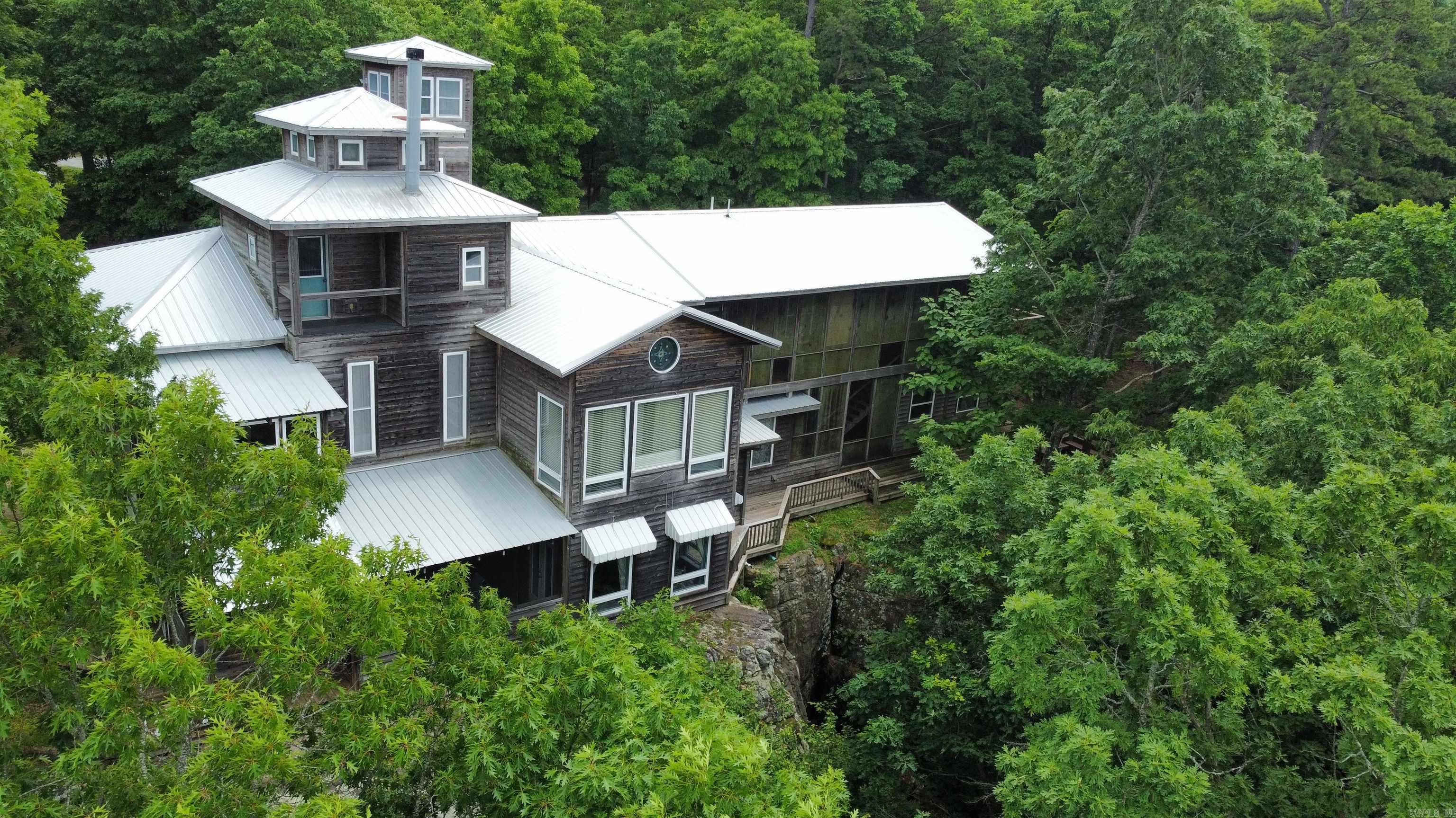 Perched high on a bluff with sweeping views of the majestic Ozark Mountains, this extraordinary estate offers luxury, privacy, and panoramic natural beauty. This expansive home is a true sanctuary, featuring a stunning lap pool perfect for morning swims, a grand great room with soaring ceilings and floor-to-ceiling windows, and a spacious living room ideal for entertaining or quiet evenings in. The gourmet kitchen is a chef’s dream with top-of-the-line appliances, generous counter space, custom cabinetry and stained glass throughout the house! Enjoy cinematic experiences in the private movie theater or unwind with a good book in the cozy reading room or elegant library. A whole-house sound system ensures your favorite music follows you from room to room. Ascend the lookout tower for breathtaking 360-degree views or descend the private staircase that winds down the bluff to a peaceful creek below. This one-of-a-kind mountain retreat blends refined luxury with the tranquil beauty of the Ozarks—an unforgettable place to call home.