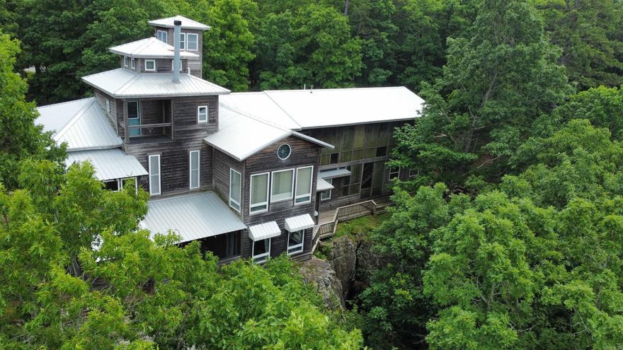 Perched high on a bluff with sweeping views of the majestic Ozark Mountains, this extraordinary estate offers luxury, privacy, and panoramic natural beauty. This expansive home is a true sanctuary, featuring a stunning lap pool perfect for morning swims, a grand great room with soaring ceilings and floor-to-ceiling windows, and a spacious living room ideal for entertaining or quiet evenings in. The gourmet kitchen is a chef’s dream with top-of-the-line appliances, generous counter space, custom cabinetry and stained glass throughout the house!   Enjoy cinematic experiences in the private movie theater or unwind with a good book in the cozy reading room or elegant library. A whole-house sound system ensures your favorite music follows you from room to room. Ascend the lookout tower for breathtaking 360-degree views or descend the private staircase that winds down the bluff to a peaceful creek below. This one-of-a-kind mountain retreat blends refined luxury with the tranquil beauty of the Ozarks—an unforgettable place to call home.