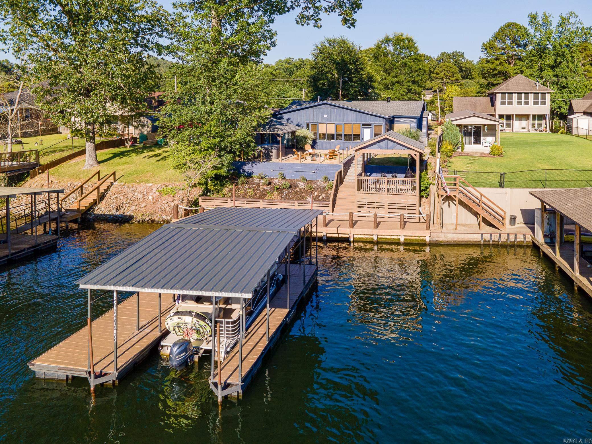 Beautiful Lakefront Home fully furnished and with active STR permit on Lake Hamilton on the River side of Ouachita River - 4 BR | 2 BA 1,750 Sq Ft - Sleeps 12 | Private Boat Dock & Hot Tub | Fire Pit Fish right off the boardwalk! The crystal clear waters allows easy sighting of trout, striped bass & striper. This charming property was established as a Vacation Rental. It is nestled on the picturesque Lake Hamilton in Hot Springs, AR, just a short distance from Blakely Mountain Dam. Relax and unwind in the private backyard, where you can gather around the fire pit or luxuriate in the hot tub. The endless summer nights outside fishing off the private deck with undoubtedly make unforgettable memories. Whether you're seeking a peaceful lake getaway or eager to explore all that Hot Springs has to offer, this cozy hideaway will not disappoint. This 1750 sq ft home boasts 4 bedrooms and 2 bathrooms, offering a comfortable retreat for your stay. The private outdoor covered patio includes a relaxing fire pit area. The property also includes a private dock, ample parking for cars and boat trailers. Outdoor patio provides a peaceful retreat with swinging chairs and a fire pit area.