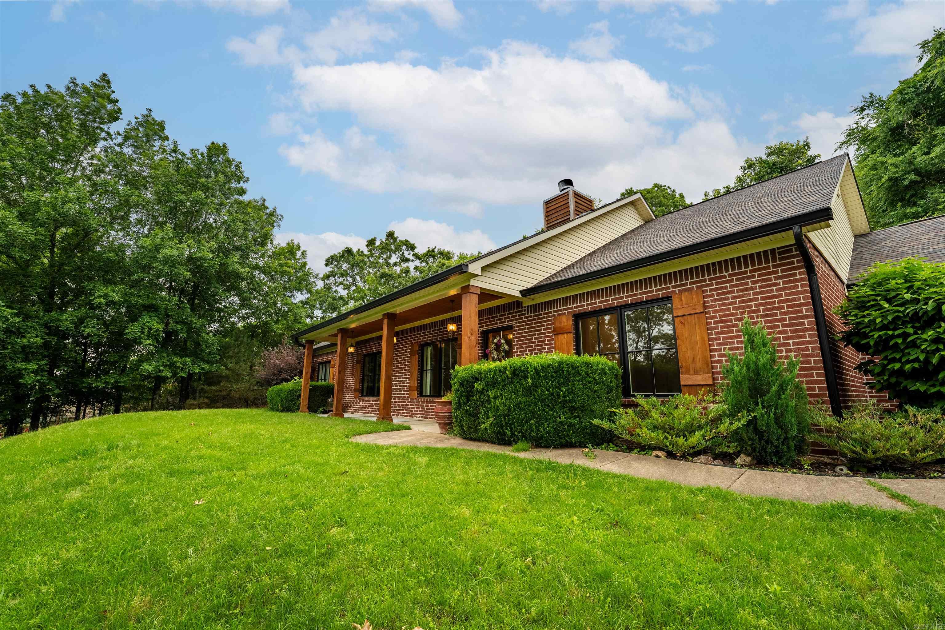 This immaculate 4 Bed, 2 Bath oasis sits atop Bald Eagle Dr with stunning views of the Ouachita Mountains. A private tree-wrapped circular drive welcomes you to a charming covered patio and elegant Marvin Signature wood & mahogany doors/windows. Inside, the vaulted great room boasts a stone wood-burning fireplace and a wood-beamed kitchen with a breakfast island, custom cabinetry, smart vent-hood, stainless appliances, brick backsplash, and double doors to your private patio overlooking peaceful acreage. Follow the rock path past your campfire setup to a pool with a new liner and pump—perfect for summer days and starry nights. The private primary suite includes a walk-in shower, jetted tub, double vanities, and double closets. Through the laundry room, find an office and oversized storage closet. Three guest bedrooms share a full bath on the opposite wing. Additional features include a newer roof, updated electrical, and a 2-car garage with workshop space.