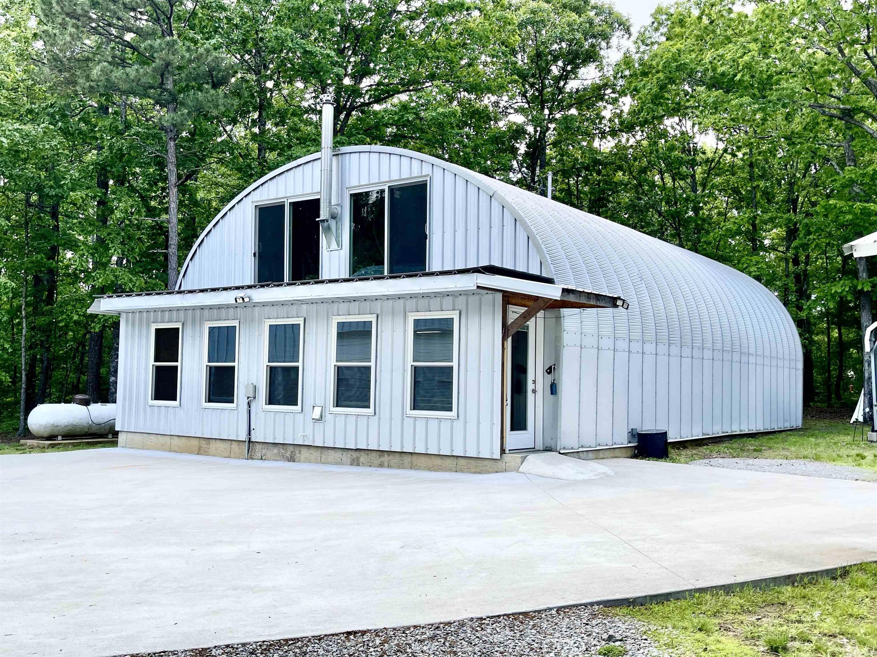 Over 5 acres of privacy and within about 15 minutes of Greers Ferry Lake! WOW!! Quonset home is 30' X 50' and has 1 1/2 stories with approximately 2200 sq ft of living space! The workshop/boat storage, etc. is even larger - 40' X 58' and also has an upstairs! House boasts a living room, den/kitchen, 2 BR and 1 bath on main floor and 1 Bedroom and 1 Bath upstairs and space for an exercise room or office! There is a large 2 car carport and 2 large shipping containers for tons of storage! There are 3 mini split units and upstairs has a woodburning stove. Gas water heaters are tankless units and windows are Low-e windows! Shop building is insulated and has water so a bathroom or kitchen could probably be added if needed. Kitchen has beautiful marble countertops. House was built in 2022 and shop building was built in 2024. You do not want to miss this one!!