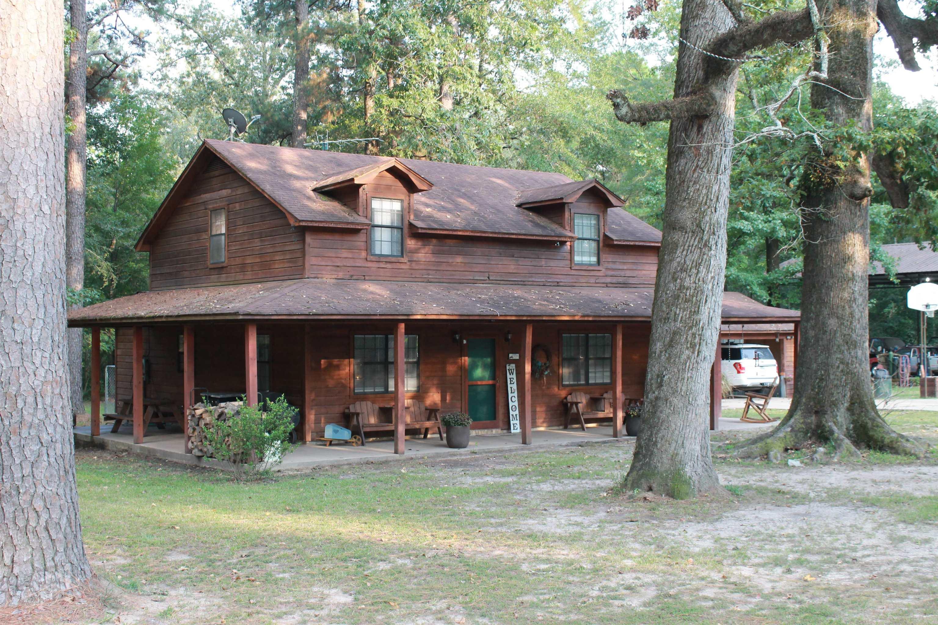 Beautiful setting with 2 story brown cedar country house situated on 3 Acres; House features den with wood burning fireplace with insert; Wrap around porch in front and 2 sides; Separate garage with cover to get into house with storage behind that could be used for office or school room; 3 bedrooms and 2 baths upstairs; Kitchen features gas range, large refrigerator, and dishwasher; 30 x 40 RV shed with concrete floor; Yard ornaments do not stay