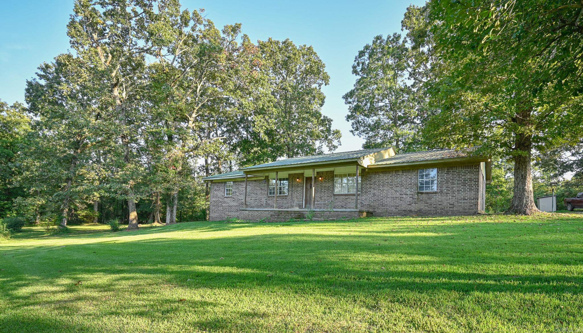 Come home to the country five minutes from Mena. Brick home is nestled among large trees, beautiful front and back yard, private yet close to Mena. Open living and dining area, built in bookshelves, spacious bedrooms, large laundry/ utility room. Covered porches and carport.