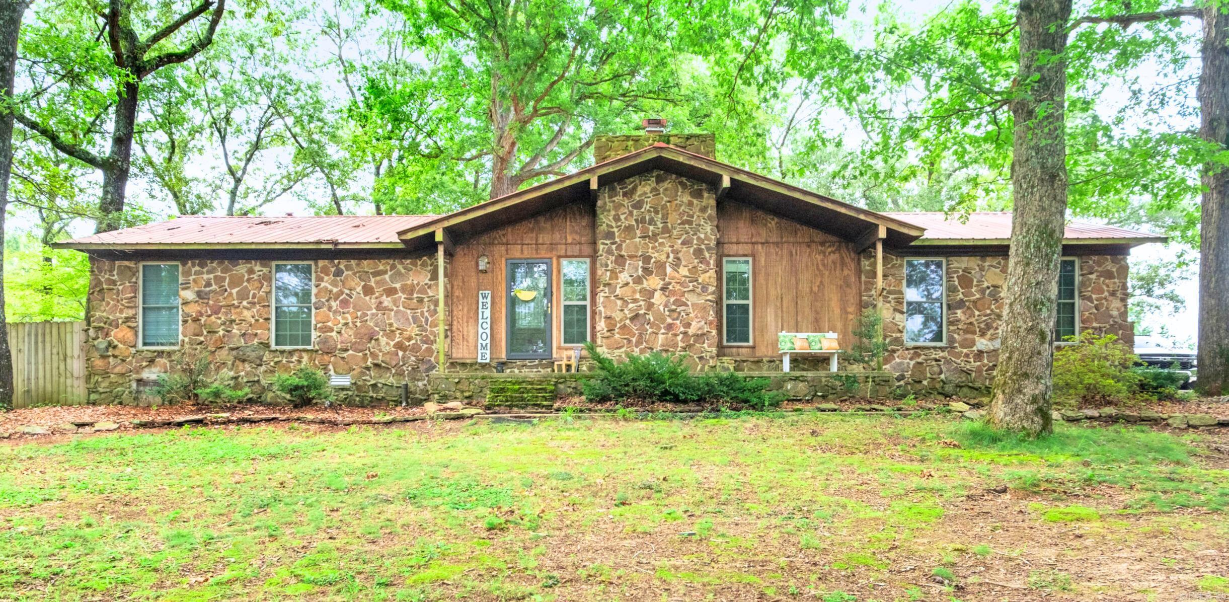 This rustic ranch-style 4-bedroom, 2.5-bath charmer sits on a private 1.1-acre lot in the Bald Knob Country Club area—just steps from the golf course and pool! Surrounded by mature trees, the home features a spacious open-concept kitchen, dining, and living area with vaulted ceilings, custom cabinetry, a large island, gas range, and plenty of storage. Enjoy beautiful wood floors, a cozy rock fireplace, and an asphalt circle drive with ample parking. A privacy fence along the side and back of the property offers added seclusion, making this a peaceful place to call home.
