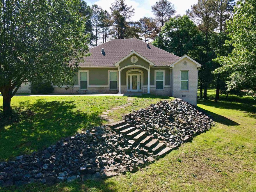 Located on nearly 3 acres in the desirable Brookhill area, 780 Brookhill Ranch Road offers privacy just minutes from the Hot Springs Village gates. This 2008 custom-built home features an open floor plan with vaulted ceilings and significant natural light from large windows and sun tubes. The interior is updated with new Green Guard Gold certified waterproof LVP flooring throughout. The kitchen includes custom cabinetry, ample workspace, and a large pantry, while the primary suite is designed with a functional office nook and a walk-in shower. Additional living space includes a heated and cooled sunroom for year-round use.  A standout feature of the property is the 60x40 detached shop with 6" thick concrete floor. This 3200 sq ft versatile building includes a partially finished, 20x40 loft equipped with full bathroom and washer hookup, making it ideal for a workshop or hobby space. The shop has an additional half bath on main level and has a heated/cooled area. This property efficiently combines a well-maintained residence with substantial utility and acreage.