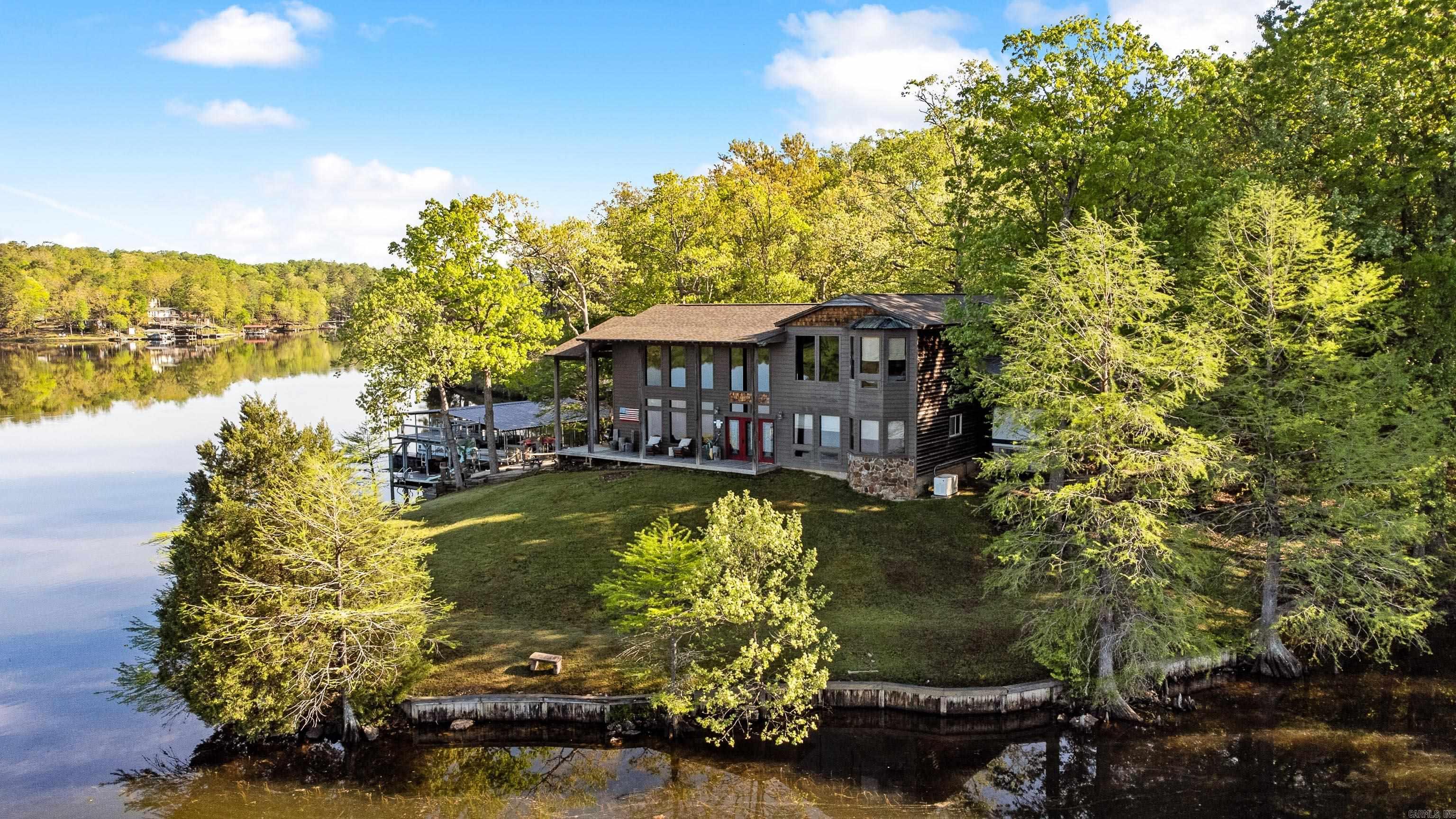 Welcome to your private lakefront retreat on 5 acres at the point of Lake Norrell, offering stunning panoramic water views. This incredible property is built for entertaining with an outdoor kitchen featuring a gas grill, bar seating, hot tub and a woodburning fireplace, plus expansive decks with a slide, diving board, and two covered boat docksāone with a lift. The big flat backyard is ideal for gatherings, complete with a covered porch boasting soaring 20 ft ceilings. Inside, youāll find two living spaces and two kitchens, each with fireplaces, and a main living room with 20 ft ceilings and intricate woodwork. The spacious kitchen offers a 6-burner gas range with double ovens, granite countertops, and a walk-in pantry. Located upstairs, the primary suite features lake views, double closets, and a large soaking tub. The two extra bedrooms and conveniently located downstairs. Extras include a whole-home generator, heated floors, safe room, built in bunk beds (easily removable) and a geothermal HVAC system, making this home as comfortable as it is breathtaking!