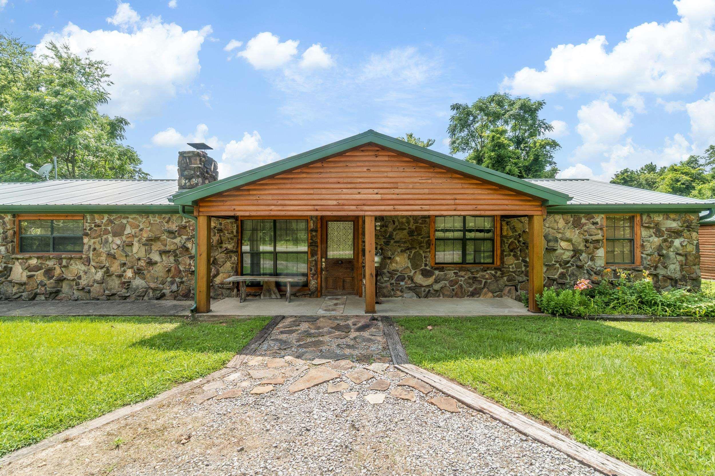 Stunning Craftsman Retreat on 5.58 Acres! with Workshop, Orchard & Creek – Experience timeless craftsmanship and serene living in this beautifully designed single-level 4-bedroom, 2-bathroom home, offering 2,200 sq ft of thoughtfully curated space. Wrapped in charming log siding and native Arkansas stone, and topped with a new metal roof & gutters, this one-of-a-kind property seamlessly blends rustic elegance with modern comfort. Step into the spacious open-concept living and dining area—perfect for entertaining—anchored by a grand stone fireplace and hearth. On the opposite wall, custom walnut cabinetry and a handcrafted hickory bookshelf create a warm, inviting library and office space, accented by hickory plank flooring that adds a touch of sophistication. Car enthusiasts, hobbyists, or those needing extra space will appreciate the 2-car garage with built-in cabinets and work counter—climate-controlled for year-round use. Additionally, a separate climate controlled 750 sq ft detached workshop/garage features a wide 16-foot door and heavy duty electric hoist for lifting and state of the art well pump system. Don't miss your chance to own this charming country retreat!