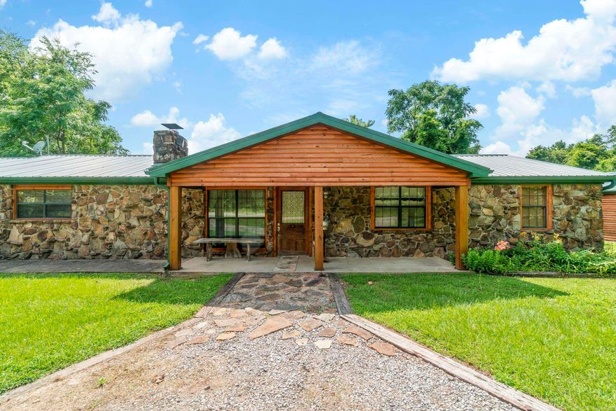 Stunning Craftsman Retreat on 5.58 Acres! with Workshop, Orchard & Creek –   Experience timeless craftsmanship and serene living in this beautifully designed single-level 4-bedroom, 2-bathroom home, offering 2,200 sq ft of thoughtfully curated space. Wrapped in charming log siding and native Arkansas stone, and topped with a new metal roof & gutters, this one-of-a-kind property seamlessly blends rustic elegance with modern comfort.  Step into the spacious open-concept living and dining area—perfect for entertaining—anchored by a grand stone fireplace and hearth. On the opposite wall, custom walnut cabinetry and a handcrafted hickory bookshelf create a warm, inviting library and office space, accented by hickory plank flooring that adds a touch of sophistication.  Car enthusiasts, hobbyists, or those needing extra space will appreciate the 2-car garage with built-in cabinets and work counter—climate-controlled for year-round use. Additionally, a separate climate controlled 750 sq ft detached workshop/garage features a wide 16-foot door and heavy duty electric hoist for lifting and state of the art well pump system.   Don't miss your chance to own this charming country retreat!