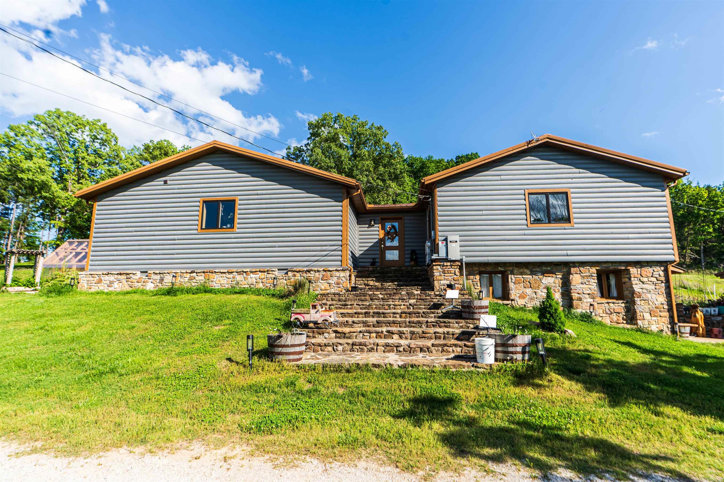 Nearly 125 acres of privacy, natural beauty, and off-grid potential await. This one-of-a-kind retreat features a spacious 3 bed, 3 bath home (approx. 2,500 sqft) with beautiful wood interiors and a restored original stone foundation from the property's earliest build. The main level includes a cozy living area, full bath, and kitchen with warm, rustic charm. Upstairs you'll find three bedrooms and two full baths, including a massive primary suite that spans over half the upper level. Don't miss out on the built-in storage throughout the primary bath! Enjoy the expansive outdoor living space with a large stone fireplace and bar—perfect for relaxing or hosting gatherings. A detached garage/workshop sits just steps away. The land is ideal for outdoor enthusiasts, with wildlife/game feeders, abundant deer and turkey, and multiple hunting stands—including 2 large enclosed stands. A freshwater spring runs year-round, with a second seasonal spring in the bluff. Solar-wired home with whole-home generator, 1,000-gal. buried propane tank, deep well, custom chicken coop, fruit trees/orchard, and a 1-mile private drive complete this private haven.