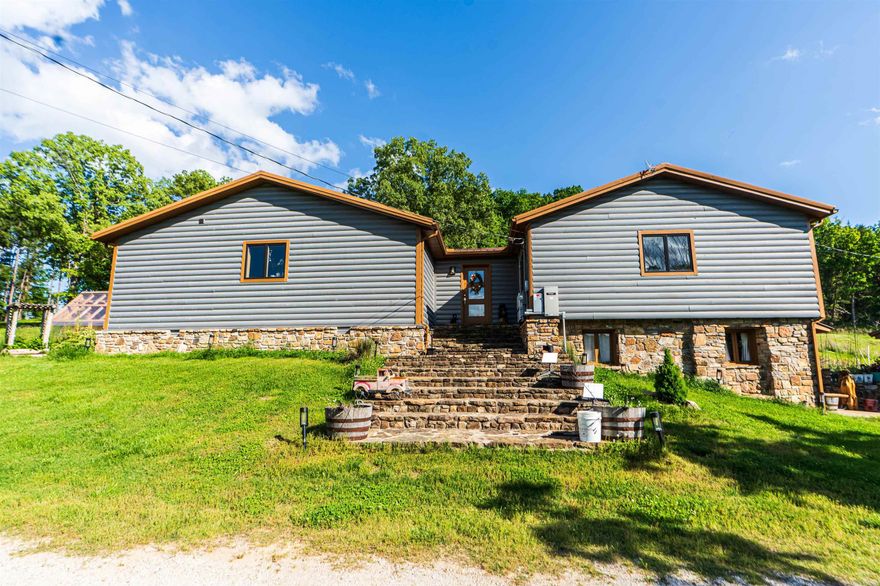 Nearly 125 acres of privacy, natural beauty, and off-grid potential await. This one-of-a-kind retreat features a spacious 3 bed, 3 bath home (approx. 2,500 sqft) with beautiful wood interiors and a restored original stone foundation from the property's earliest build. The main level includes a cozy living area, full bath, and kitchen with warm, rustic charm. Upstairs you'll find three bedrooms and two full baths, including a massive primary suite that spans over half the upper level. Don't miss out on the built-in storage throughout the primary bath!   Enjoy the expansive outdoor living space with a large stone fireplace and bar—perfect for relaxing or hosting gatherings. A detached garage/workshop sits just steps away. The land is ideal for outdoor enthusiasts, with wildlife/game feeders, abundant deer and turkey, and multiple hunting stands—including 2 large enclosed stands. A freshwater spring runs year-round, with a second seasonal spring in the bluff. Solar-wired home with whole-home generator, 1,000-gal. buried propane tank, deep well, custom chicken coop, fruit trees/orchard, and a 1-mile private drive complete this private haven.