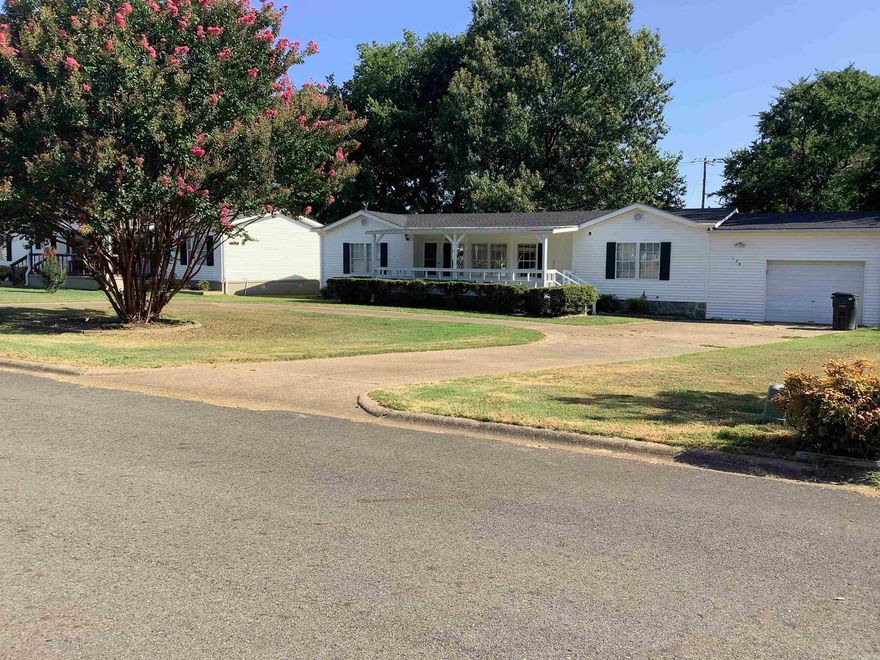 Picture yourself on this charming front porch—just add a swing and a glass of lemonade. The landscaped front yard features mature crape myrtles and manicured shrubs, set against the scenic backdrop of Mt. Riante.  Step inside to an open-concept living area with a cozy fireplace as the focal point. The kitchen boasts a breakfast bar, built-in buffet with glass-front cabinets, and a spacious walk-in pantry.  The dining area opens to a large back deck through sliding glass doors—ideal for entertaining or relaxing outdoors.  This smart split floor plan includes two generous guest bedrooms with walk-in closets and a full guest bath. The primary suite has its own walk-in closet and bath with walk-in shower and in-room washer/dryer. A door connects the bath to the garage—perfect for post-yardwork cleanup.  The oversized one-car garage includes cabinets and shelving. A back door leads to a shady yard with a dog run and a doggie door from the pantry for easy outdoor access.  Bonus: Enjoy the community clubhouse with full kitchen, pool tables, small gym, and a beautiful pool. Located in a 55+ community.  Come take a look—this might be just what you’ve been searching for!