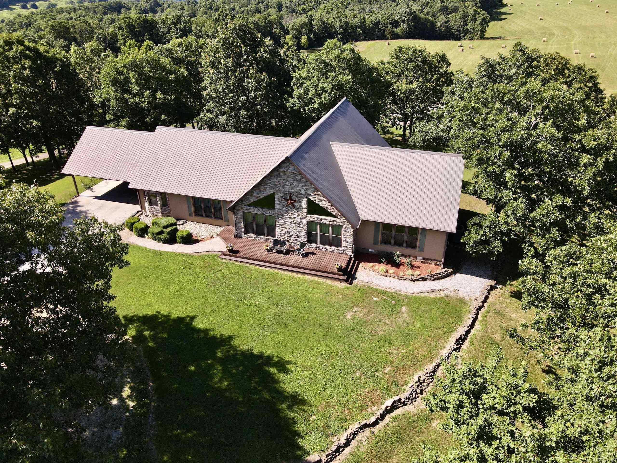 Perched atop the highest point in the county, this premier Ozark Mountain estate offers a rare combination of luxurious comfort, self-sufficient functionality, and breathtaking panoramic views. The custom-built 3-bedroom, 2-bathroom main residence spans 2,542 square feet, with expansive decks and covered porches that capture stunning sunrises, sunsets, and rolling green pastures from nearly every room. Every inch of this property has been thoughtfully maintained and masterfully developed.