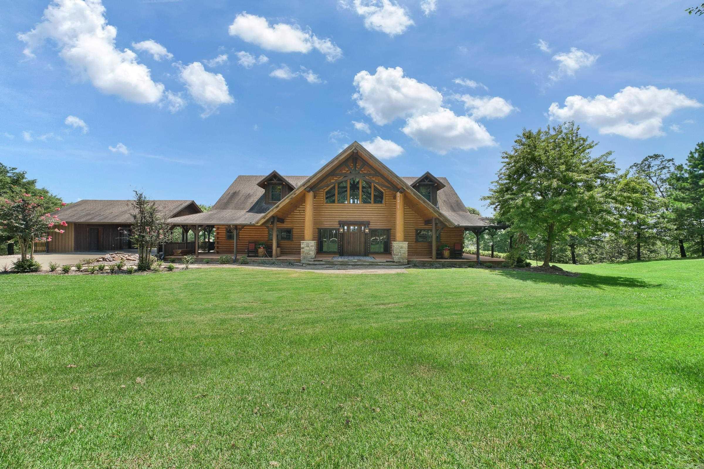 Welcome to your dream retreat by DeQueen Lake! This stunning 3,572 sqft log and stone cabin in DeQueen, AR, offers a perfect blend of rustic charm and modern comfort. The fully furnished two-story home features 4 spacious bedrooms, including one with a versatile Murphy bed, and 3.5 luxurious baths—all with double sinks. Step outside to enjoy the 1,200 sqft wrap-around porch, complete with comfy furnishings, or entertain on the expansive back deck and stone patio with a large fire pit. The property is surrounded by peaceful, forested land with a running brook, a pond, and a life-size bronze sculpture by Jo Saylor. Inside, the chef’s kitchen boasts granite countertops, stainless steel appliances, two double sinks, and two dishwashers. Additional features include a massive hand-cut stone fireplace, hand-scraped hickory wood floors, central air, electric heating, ceiling fans, and lightning protection. This rare gem offers serene views and plenty of space for relaxation and entertainment. Schedule your showing today!