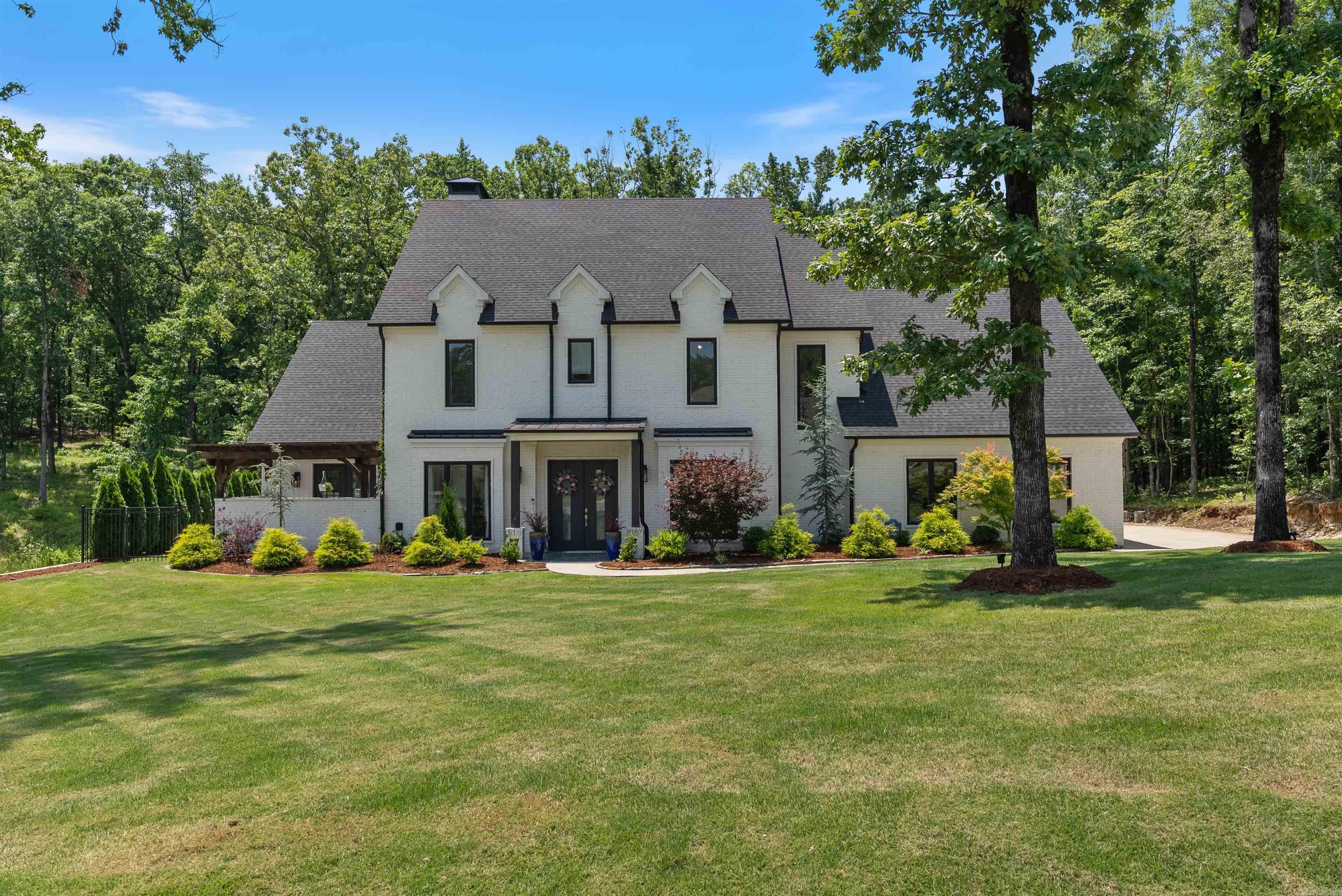This stunning custom-built home sits just outside the Little Rock city limits on nearly an acre in a private, wooded neighborhood—offering peaceful seclusion without sacrificing city conveniences. Inside, the entry opens to an office with French doors and a formal dining room. The two-story great room boasts custom built-ins, wood beam accents, and a wood-burning fireplace with gray stone exterior. The gourmet kitchen features Quartzite countertops, a gas cooktop, double ovens, a smart refrigerator, custom Duke cabinetry with soft-close drawers, an island with bar stool seating, breakfast room, and walk-in pantry. The main-level primary suite opens to a serene courtyard and includes a spa-like bath with double sinks, wet area with walk-in shower and soak tub, private water closet, and walk-in closet. A guest suite with private bath is also on the main level. Upstairs features a landing with seating area, another guest suite, and two bedrooms with a shared bathroom. The backyard is an oasis with a saltwater pool, spa, covered patio with dedicated grill area—all surrounded by mature trees. Additional features include a three-car garage, amazing storage plus more!