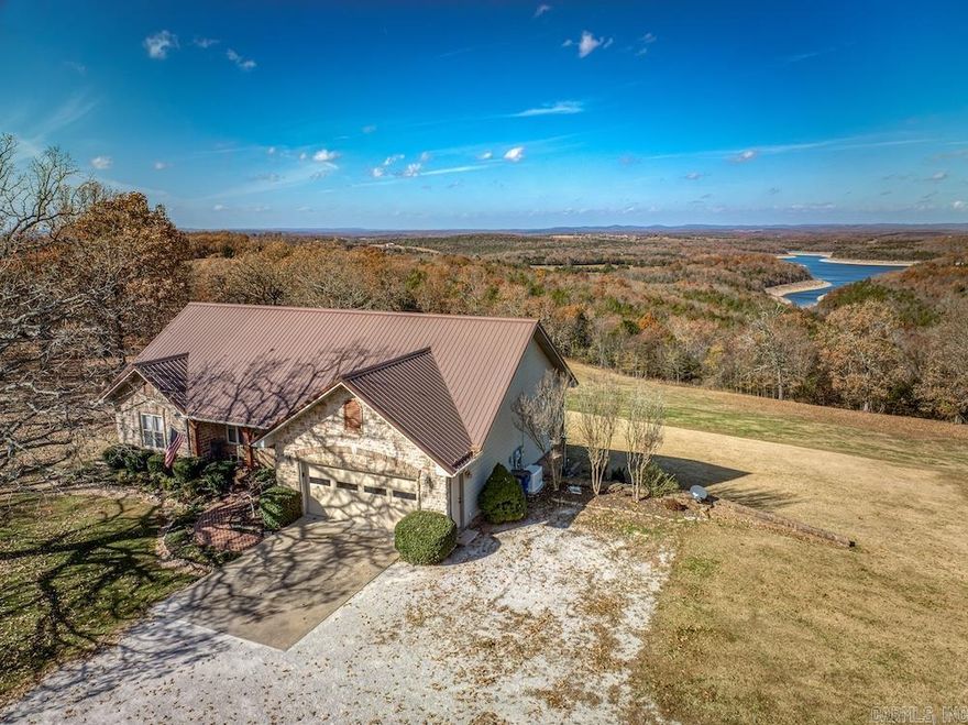 Nestled in the heart of the Ozarks and overlooking Bull Shoals Lake, this custom home sits on six serene acres just minutes from Diamond City. The park-like setting features mature oaks, a manicured yard, and a welcoming exterior of rock, brick, and vinyl with a metal roof. Enjoy a main-level two-car garage, lower-level garage, a large “forever decking” lakeview deck, and full concrete patio. Inside, the open, light-filled main level offers a custom kitchen with granite, a cozy living room with lake views and a gas fireplace, a private guest area, and a spacious master suite with dual closets and a marble walk-in shower. The finished walk-out basement includes a kitchenette, bedroom, bath, and heated/cooled oversized garage. A 24kW Generac generator, propane tank, and RV hookups add convenience. The impressive custom metal shop features three bay doors, office space, a lift, loft, concrete floors, and dog pens. Abundant wildlife and close proximity to boat ramps and marinas make this an exceptional full-time home or lake retreat.