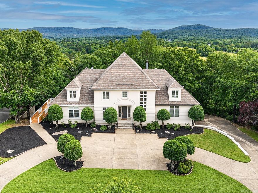 Perched on one of the highest points in Hot Springs, this exceptional custom 3-story estate sits on over an acre at the end of prestigious Whispering Hills. Featured in At Home Arkansas for its architectural design! A dramatic two-story curved window wall frames sweeping mountain views, while the sunken family room creates an unforgettable arrival. Offering 5 BR, 5.5 BA, , the home includes 2 main-level ensuite BRs, 3 upstairs BR, and a beautifully finished lower level with a game room, craft room, media space, kitchenette, and full bath. The serene primary suite features dual vanities, dual closets, a spacious shower, and soaking tub. The chef’s kitchen is appointed with a large island, custom cabinetry, and all new premium top of the line appliances, including wine fridge. Hardwood floors, plantation shutters, abundant storage, a deck with ramp access, and a 3-car garage with built-ins and epoxy flooring complete this remarkable residence. Two washers, two dryers, and the butler pantry refrigerator convey.