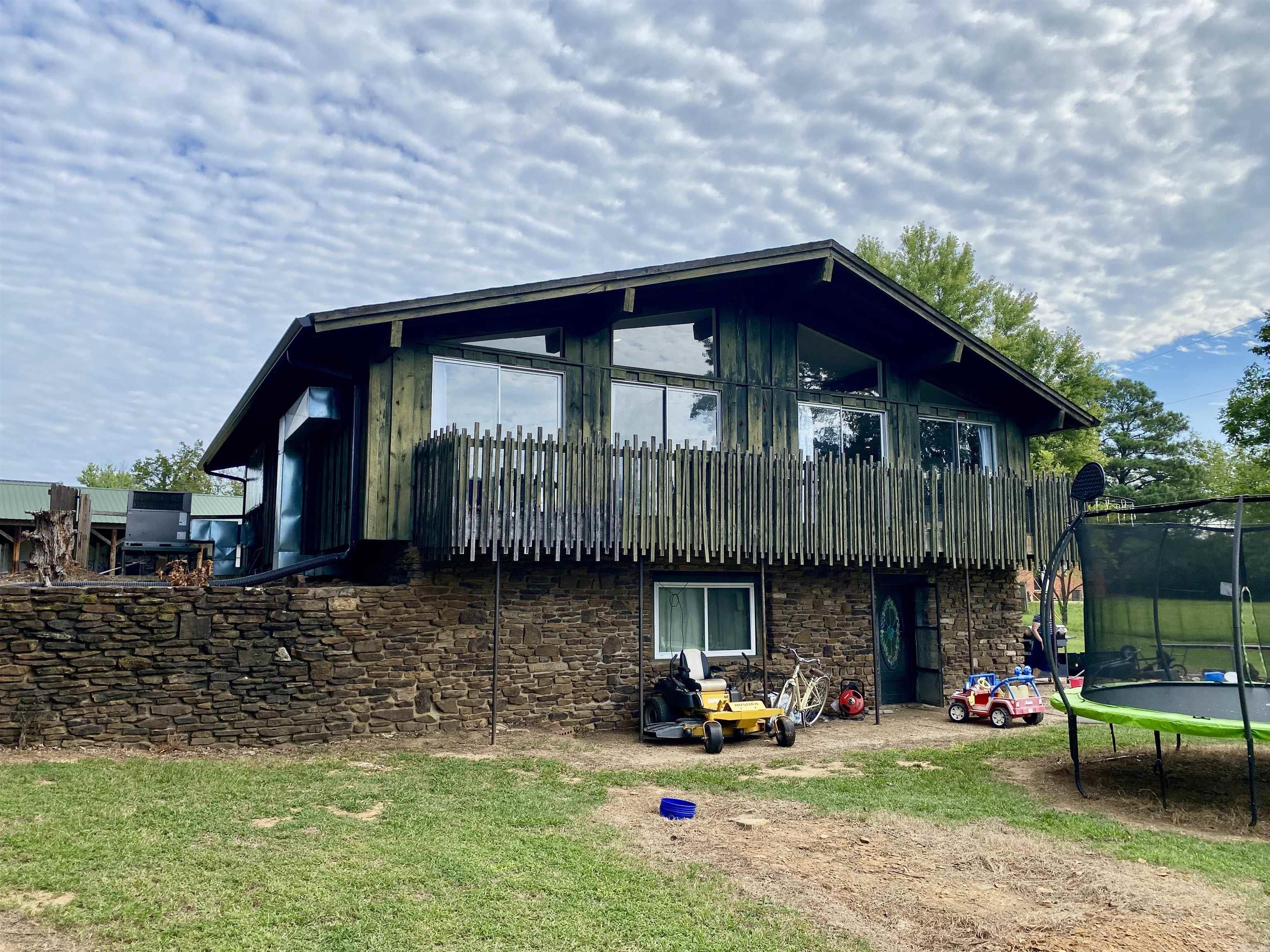Modern lines and timeless character define this 1972 home, showcasing vaulted ceilings, walls of windows, exposed wood beams, and a striking central rock fireplace that anchors both levels. The open, airy design gives off mid-century modern vibes, enhanced by wood siding and a balcony overlooking the lush 1.65-acre lawn. Recent updates include a refreshed main bath, new flooring, and a roof thatās approximately five years old. The lower level offers a spacious den/family room/master suite with an adjoining bath featuring a custom rock walk-in shower and convenient walk-out access to the backyard. A huge patio provides the perfect space for entertaining, or the flexibility to add a garage if desired. A storage building is included, and while the home needs only minor repairs, it presents a rare opportunity to add your own finishing touches to a truly unique property.