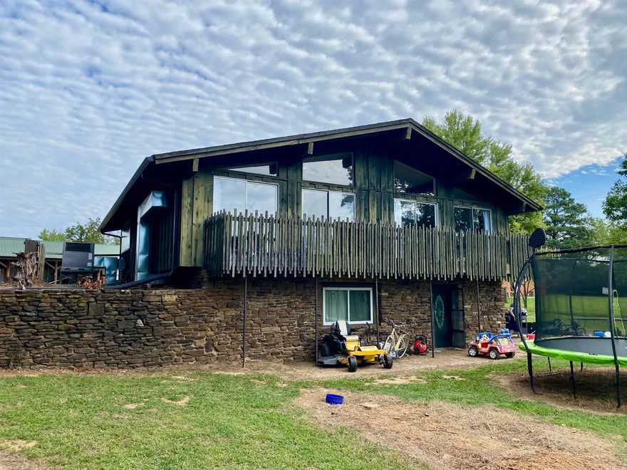 Modern lines and timeless character define this 1972 home, showcasing vaulted ceilings, walls of windows, exposed wood beams, and a striking central rock fireplace that anchors both levels. The open, airy design gives off mid-century modern vibes, enhanced by wood siding and a balcony overlooking the lush 1.65-acre lawn.  Recent updates include a refreshed main bath, new flooring, and a roof that’s approximately five years old. The lower level offers a spacious den/family room/master suite with an adjoining bath featuring a custom rock walk-in shower and convenient walk-out access to the backyard. A huge patio provides the perfect space for entertaining, or the flexibility to add a garage if desired.  A storage building is included, and while the home needs only minor repairs, it presents a rare opportunity to add your own finishing touches to a truly unique property.
