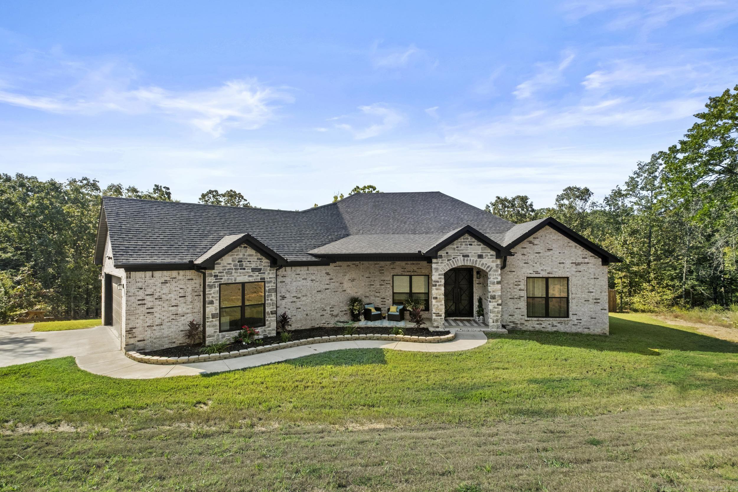 Welcome to this Stunning 2,300 sq. ft. brick home, Built in 2023 and set on 2.3 Beautifully landscaped acres in a Gated community. From the Moment you arrive, the Rock column entryway and custom Iron front door make a Bold first impression, setting the tone for the Quality and detail found throughout! Inside, the open floor plan Flows across Luxury vinyl plank flooring, anchored by a Stone fireplace and elevated with Stylish fixtures. The chef’s Kitchen is both functional and Elegant, featuring Gorgeous countertops, a Hidden walk-in pantry, Microwave drawer, Pot filler, and a Spacious eat-in breakfast bar. The luxurious Primary suite feels like a Spa retreat with a Soaking tub, Huge walk-in shower, and Designer touches throughout. Thoughtful details continue into the Laundry room, where you’ll find a Convenient sink, Stylish tilework, and Smart design that makes daily tasks easier. Step outside to enjoy your mornings or evenings on the covered Patio, overlooking your Private, tree-lined Acreage. This is more than Just a house, its a place to Gather, relax and Create lasting memories. A place to Call home. Priced below appraised value! Book your showing today! Agents see remarks.