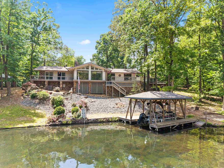 RARE FIND: All-on-one-level Lake DeSoto Waterfront! This 3BR/3BA gem features a massive open-concept great room anchored by dramatic cathedral ceilings and elegant engineered hardwood floors. UPDATED: Enjoy the peace of mind of having a new roof, newer HVAC(x3), oversized water heater, and modern kitchen appliances! The split floor plan is great for guests or multi-generational living (Bedroom 2 has a full ensuite with jetted tub!) with a gridded glass door that closes off that wing of the home. RELAX: The massive primary bedroom boasts dual sliding glass doors overlooking the lake, its own fireplace, and an ensuite with walk-in closet! The oversized tile recreation room and wet bar could be used many ways - A rec room for an Airbnb, man cave, 4th bedroom, etc. The Arkansas Room is the crown jewel of the home with a combined 4 sliding doors serving as windows overlooking the lake and deck area! FUN: The outdoor living is unmatched, featuring an entertainment-sized deck with a built-in BBQ station, quality boat dock with lift, and waterfall feature that draws from the lake! Don’t miss the huge walk-in workshop + storage room under the rear deck — perfect for lake life gear!