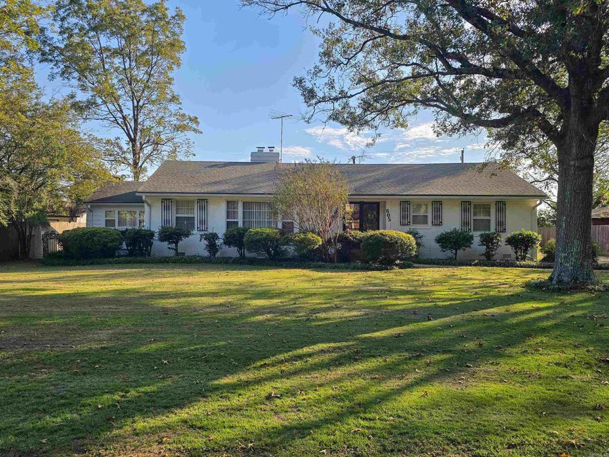 Spacious and full of charm, this 3-bedroom, 3-bath home offers an impressive layout with multiple living areas and excellent storage. The formal living room welcomes guests with large picture windows, crown molding, and its own cozy fireplace. The formal dining room features a stunning waterfall mural for a one-of-a-kind backdrop when entertaining. The kitchen offers extensive cabinets, counter space, built-in breakfast bar, large pantry, and a 3-compartment sink plus a bar sink. A convenient laundry closet is nearby. The oversized primary bedroom includes a walk-in closet and private bath, while the additional bedrooms each have great closet space and character. The massive den showcases rich wood built-ins and a large brick woodburning fireplace. Step outside to an extra-large patio overlooking the tree-shaded yard with beautiful tulip trees. Dual 11x8.5 storage rooms under the carport offer space for tools or hobbies. A Generac generator provides peace of mind. A truly extraordinary home with timeless appeal.