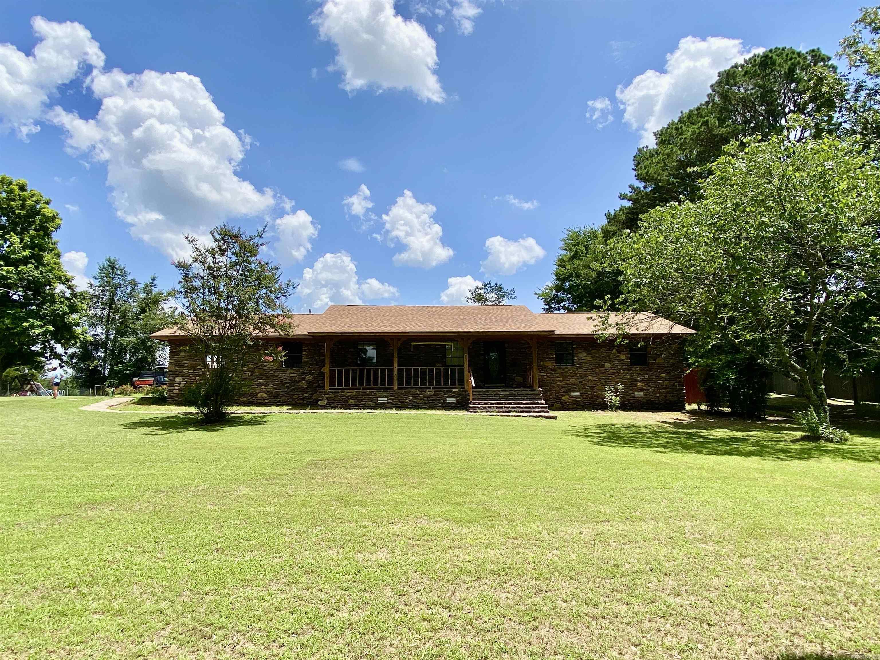 Nestled in a highly desired location just minutes from Clarksville & Lake Ludwig, this well maintained home offers the perfect blend of comfort, character, & convenience. Set on a lush lawn with established shade trees, the property features meadow & mountain views from the back lawn that provide a serene & picturesque setting. The rock exterior is complemented by a stately covered front porch, a massive matching stone fireplace, & sunroom-style flooring that fills the home with warmth & light adding an additional 273 sq.ft of living space. Inside, the inviting living area is accented by wood beams & anchored by the impressive fireplace—perfect for cozy gatherings. The fully equipped kitchen boasts solid wood cabinetry & connects to a spacious laundry area for added functionality. A new roof (installed 3 years ago) & a 2018 HVAC system offer peace of mind, while the carport, outbuilding, & double garage with storage add plenty of space for vehicles, tools, & hobbies. Additional 1.25 acres and barn available for an additional $10,000.